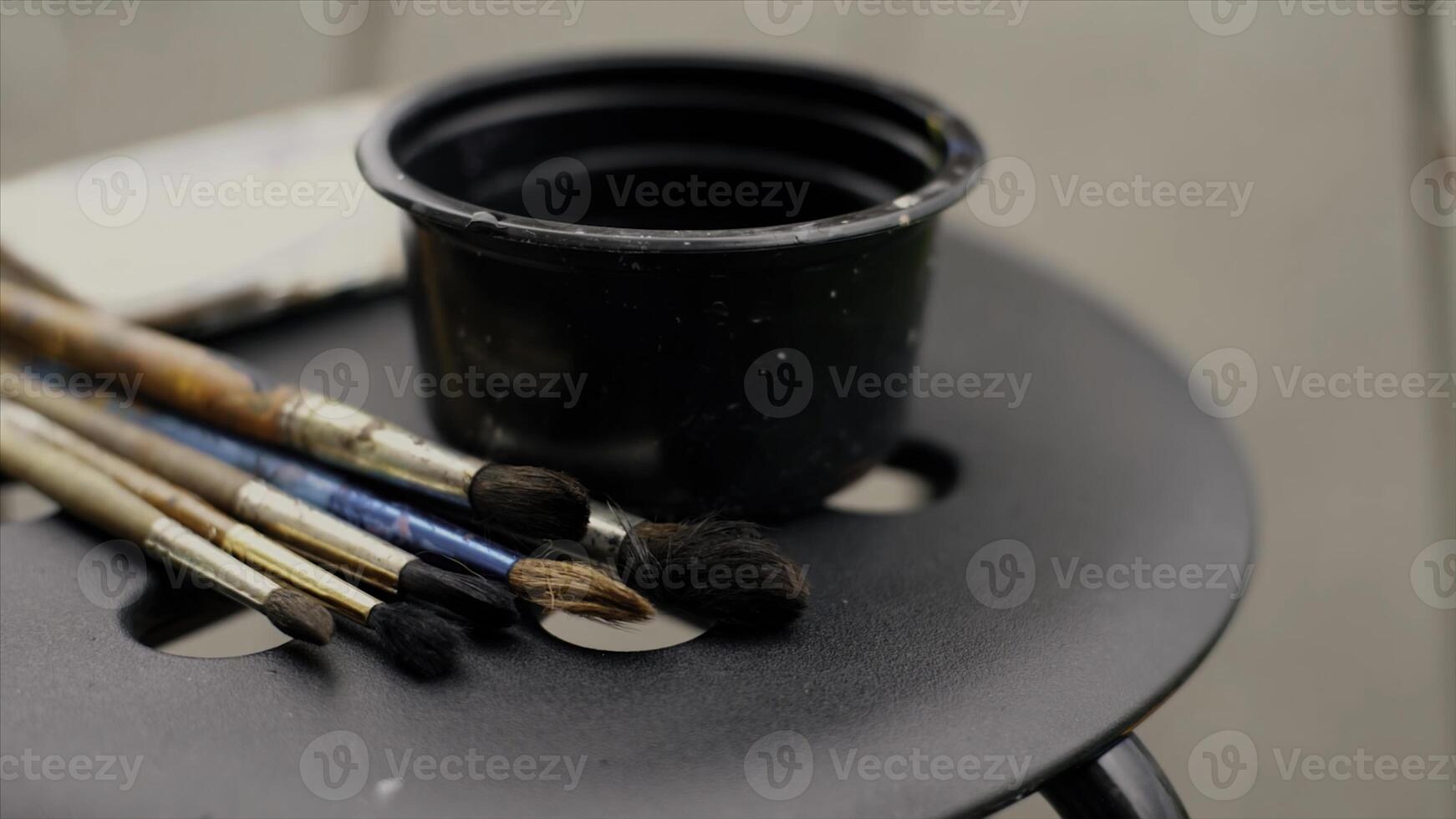 Close up of paint brushes with colorful stains and a small cup of water on a chair. Video. Concept of art and creativity. photo