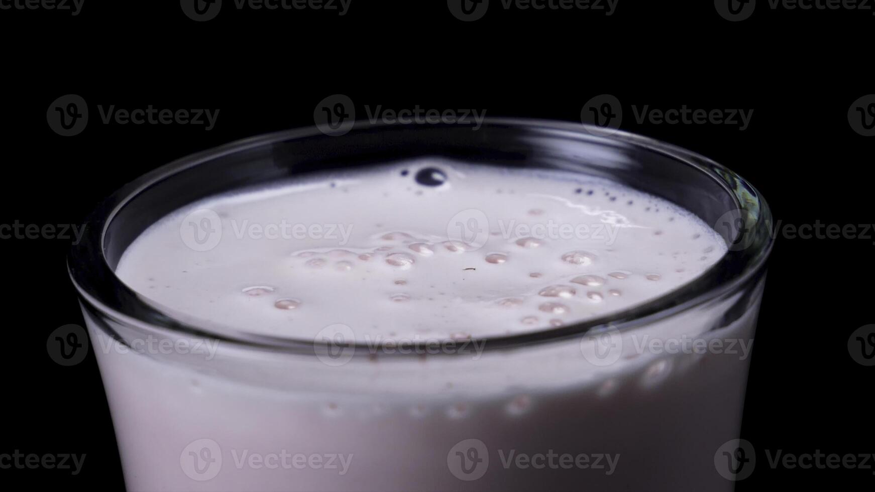 Close-up of glass with strawberry milkshake. Frame. Freshly whipped pink milkshake in clear glass on black isolated background photo