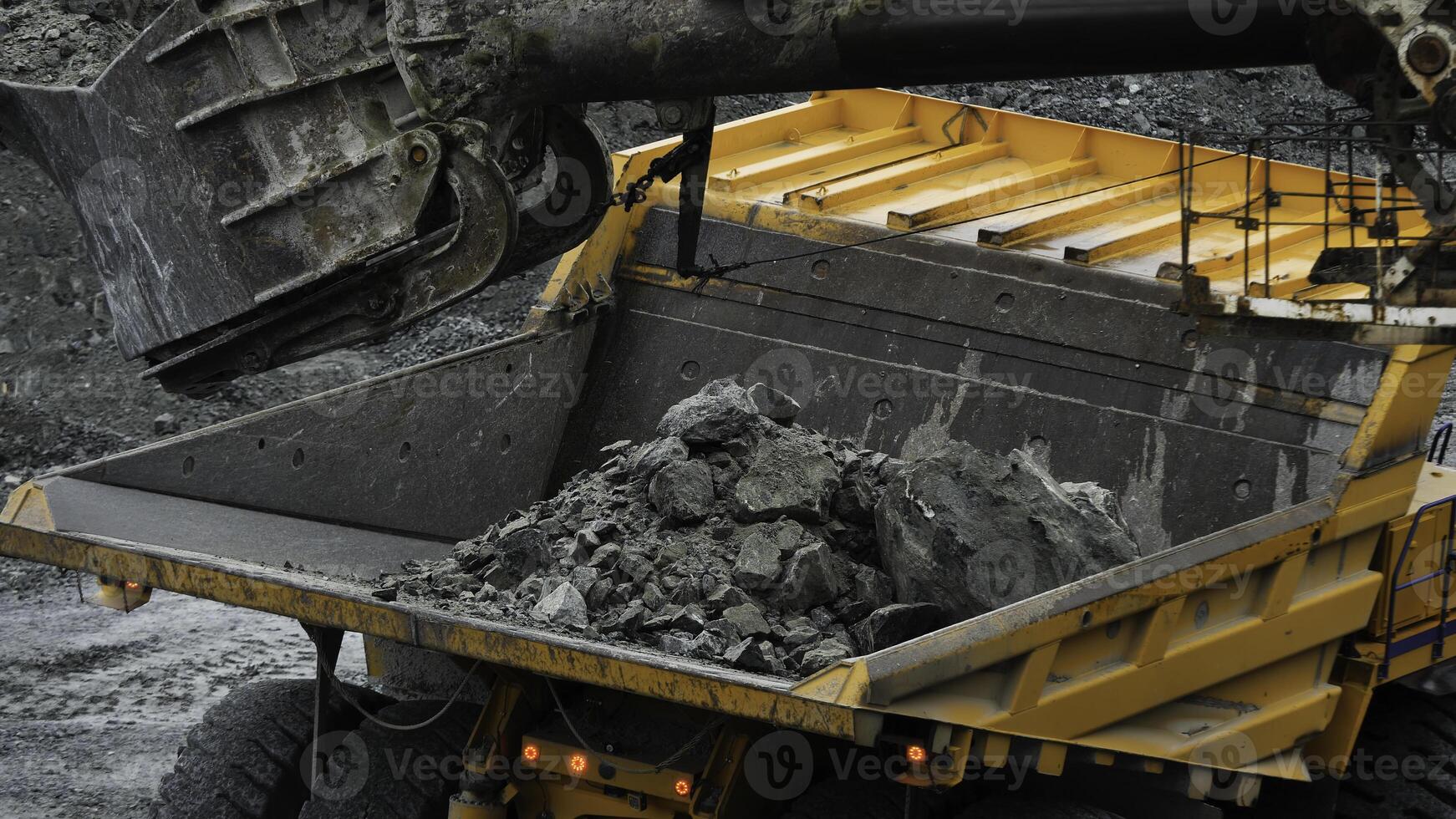 Excavator fills dump truck. Bucket excavator closeup loads stones into body of dump truck on mining or construction of something photo