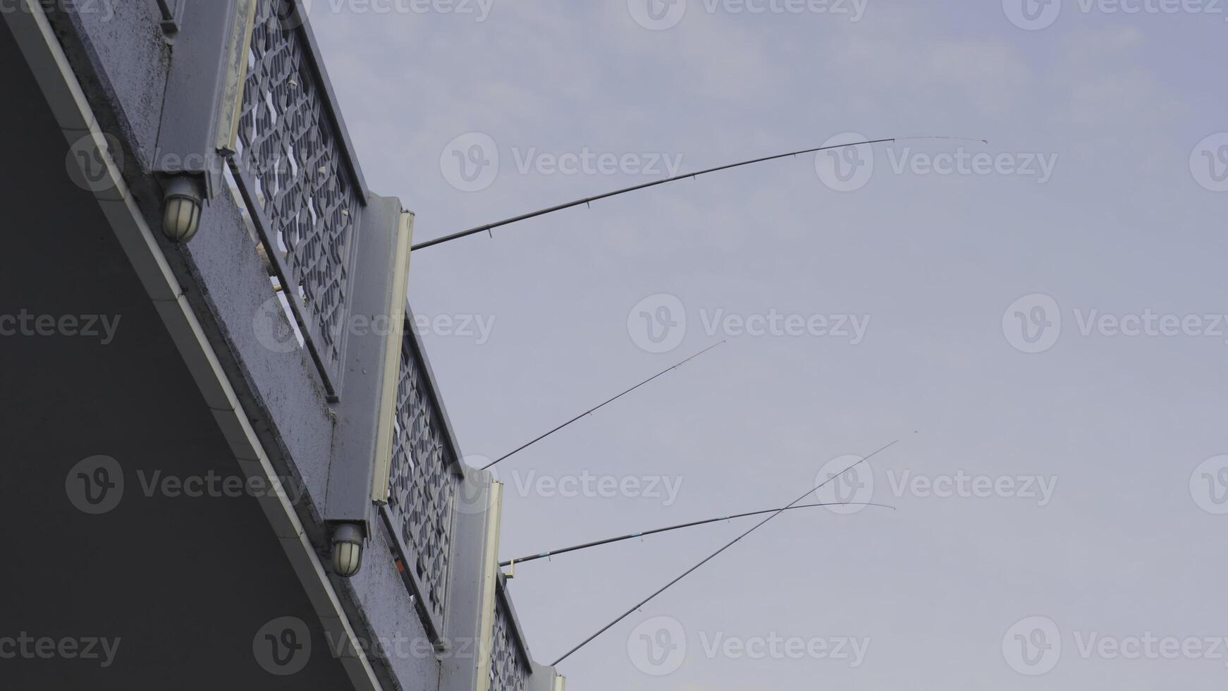 Fishing rods on bridge. Action. Bottom view of fishing from city bridge. Turkish fishermen fish from bridge on sunny day. Fishing rods on bridge on background of blue sky photo