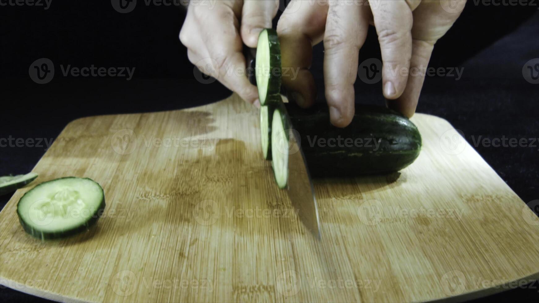 Close-up of man's hands cutting a fresh cucumber on a wooden board at the restaurant kitchen in slow motion. Stock footage. Concept of high quality food. photo