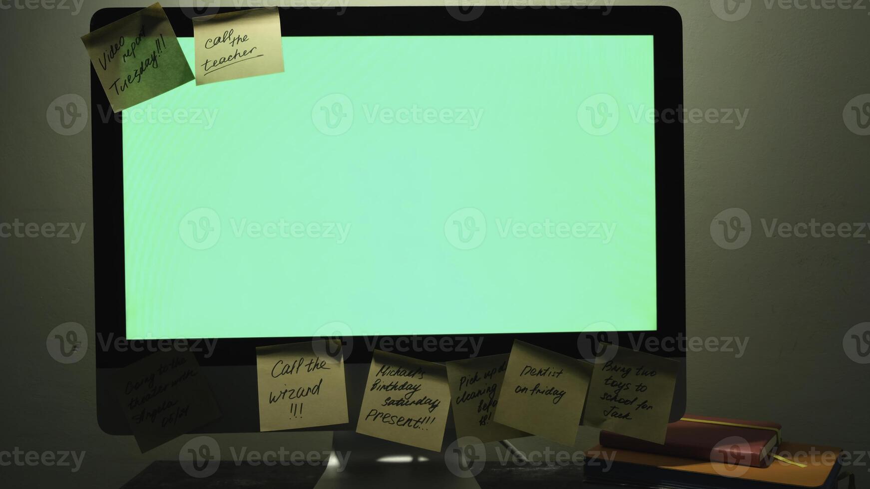 Close up of modern working place with a chromakey screen computer, daily planners and post it notes. Concept. Female hand glueing a sticker note on a computer with green screen. photo