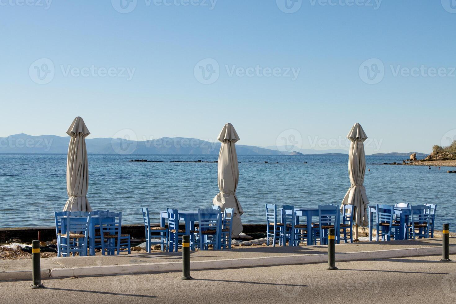 Open air Cafe on the seashore with blue chairs and folded umbrellas in Aegina, Greece photo