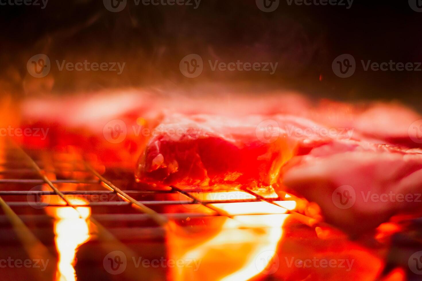 Grilling pork on stainless steel grill with flames on black background, food and cuisine concept. Burning pork on a charcoal grill. photo