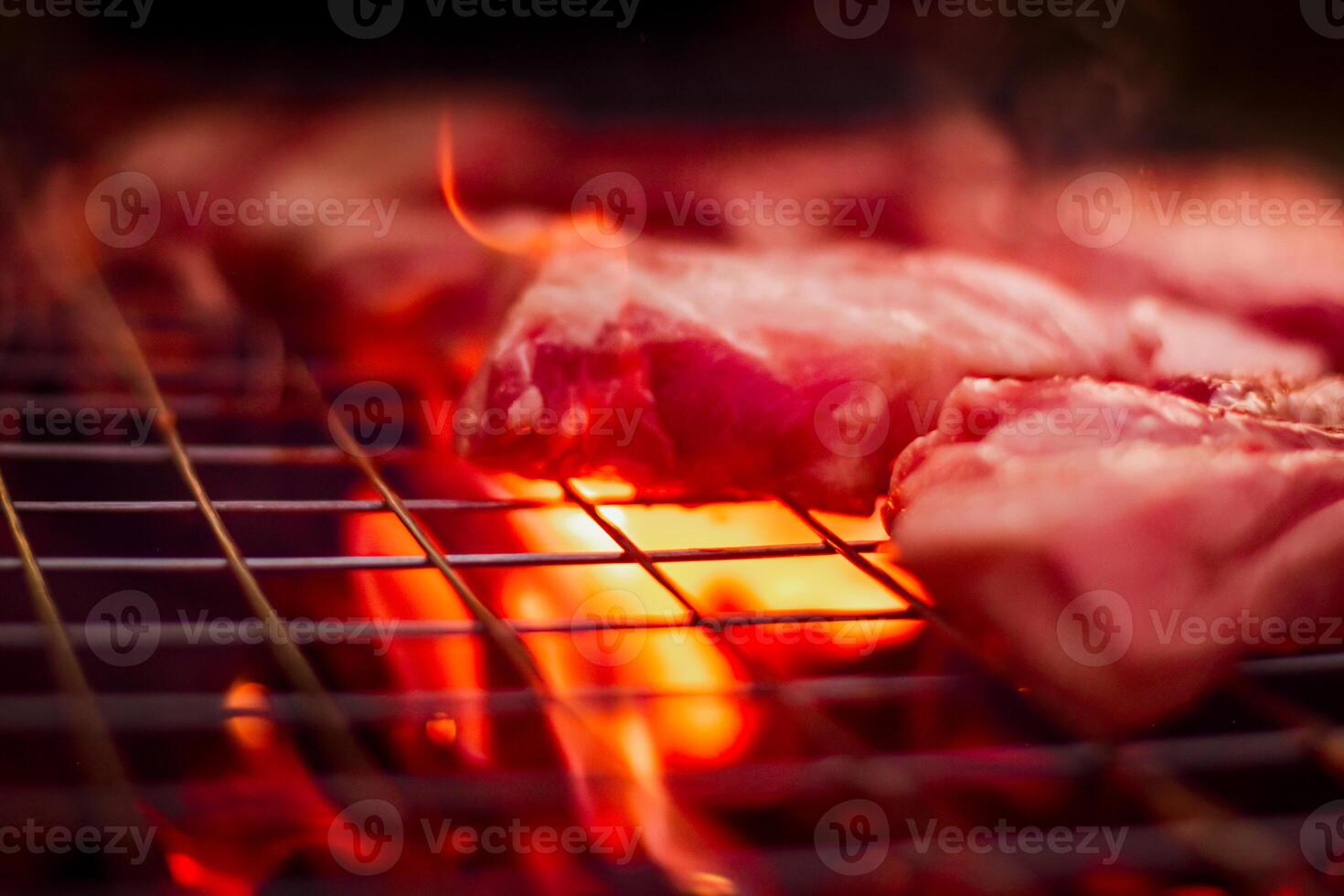 Grilling pork on stainless steel grill with flames on black background, food and cuisine concept. Burning pork on a charcoal grill. photo