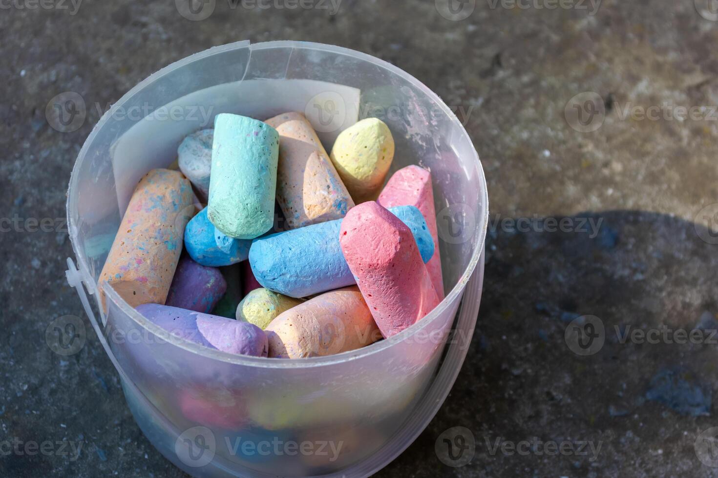 Multi colored crayons in an old broken bucket on a concrete background. photo