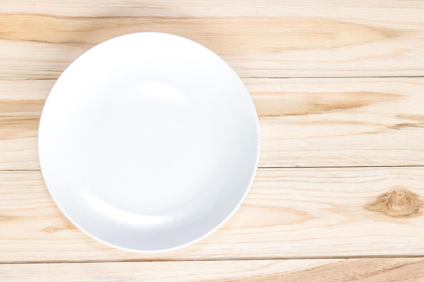 Empty white plate on light wood table for copy space and texture photo