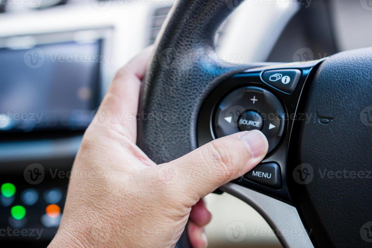 cerca arriba mano un conductor prensa el multifunción botón de coche en el direccion rueda utilizar controlar audio y cambio jugador música foto