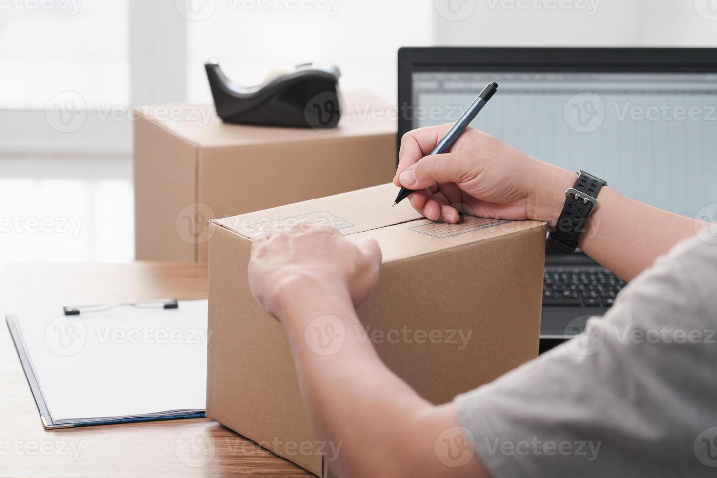 Close up hand a man use pen write on parcel box about the parcel delivery address and use laptop to register in the online system photo