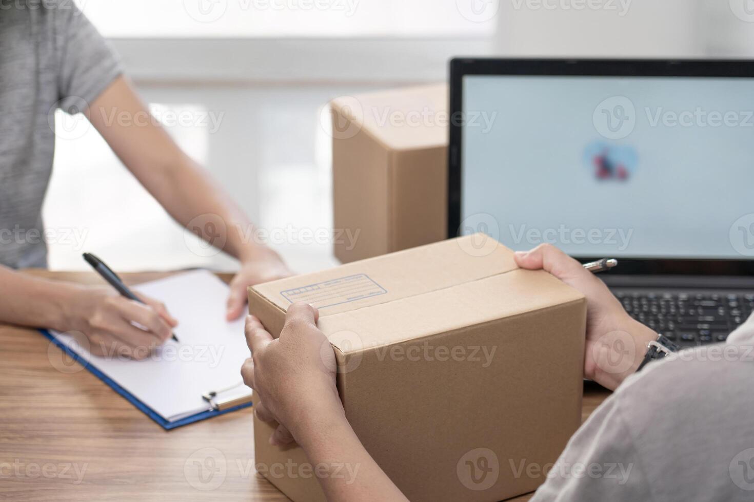 Parcel officer man hold Parcel box from women and use laptop to register in the online system to send parcels and women write the document delivery address in the form of the parcel delivery photo