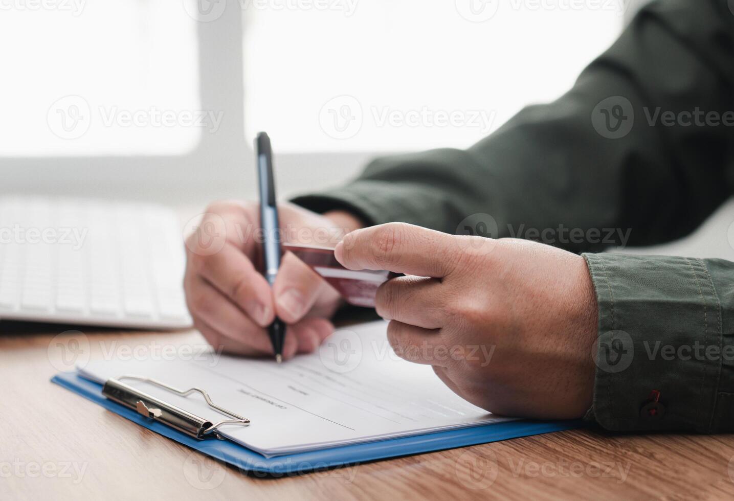 Businessman hold credit card in hand for make online banking, making a payment or purchasing on the internet entering memo details on note book and laptop computer on table photo