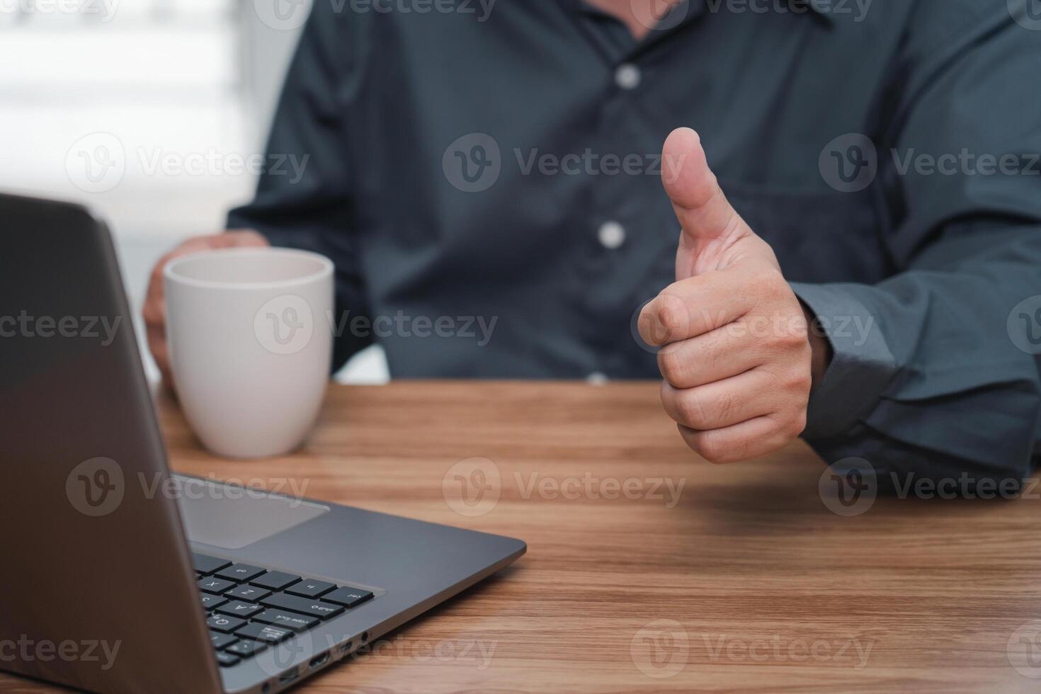 Close up hand a man thumbs up and drink coffee for work on the project successfully using computer and writing on a paper on desk in office photo