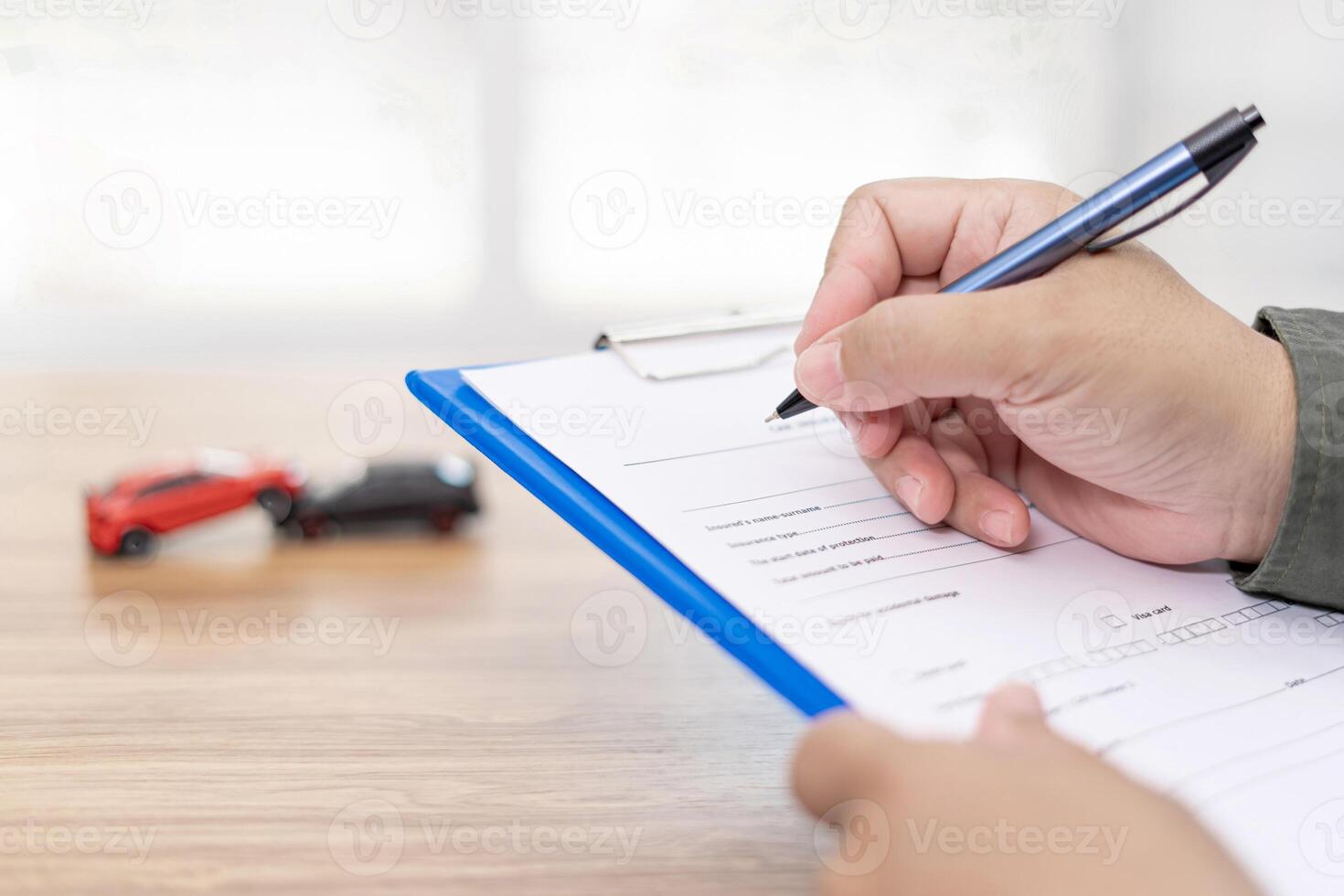 Car insurance concept  A man use a pen write insurance document on table and accident toy car model concept on wood table photo