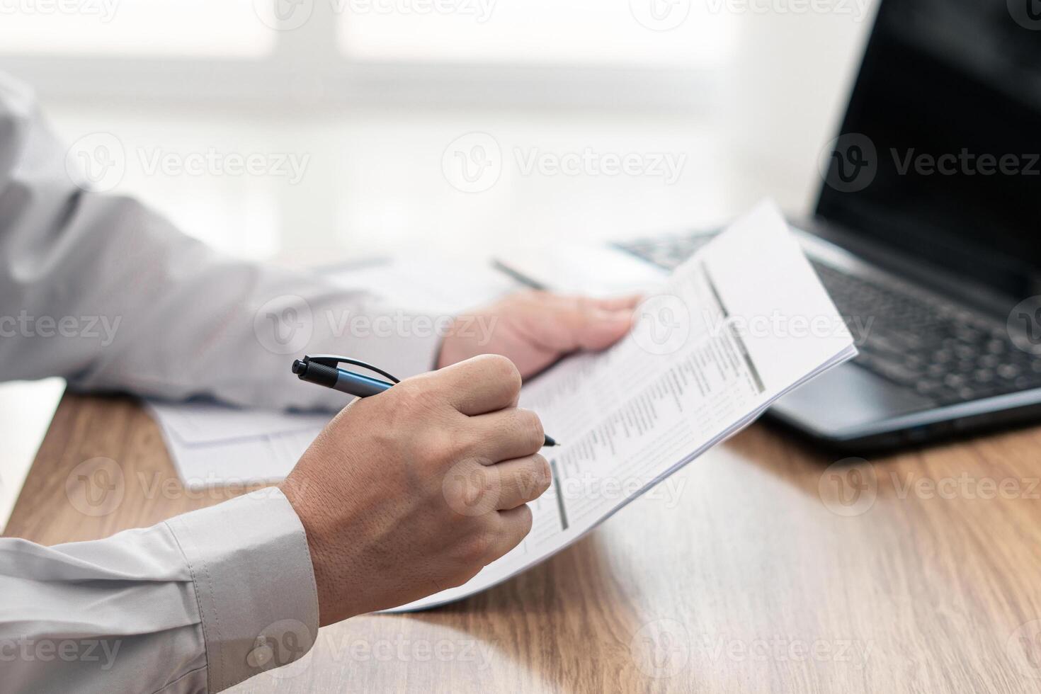 A man use pen write on the checklist paper check service list in office with repair part of car and laptop computer on wood table photo