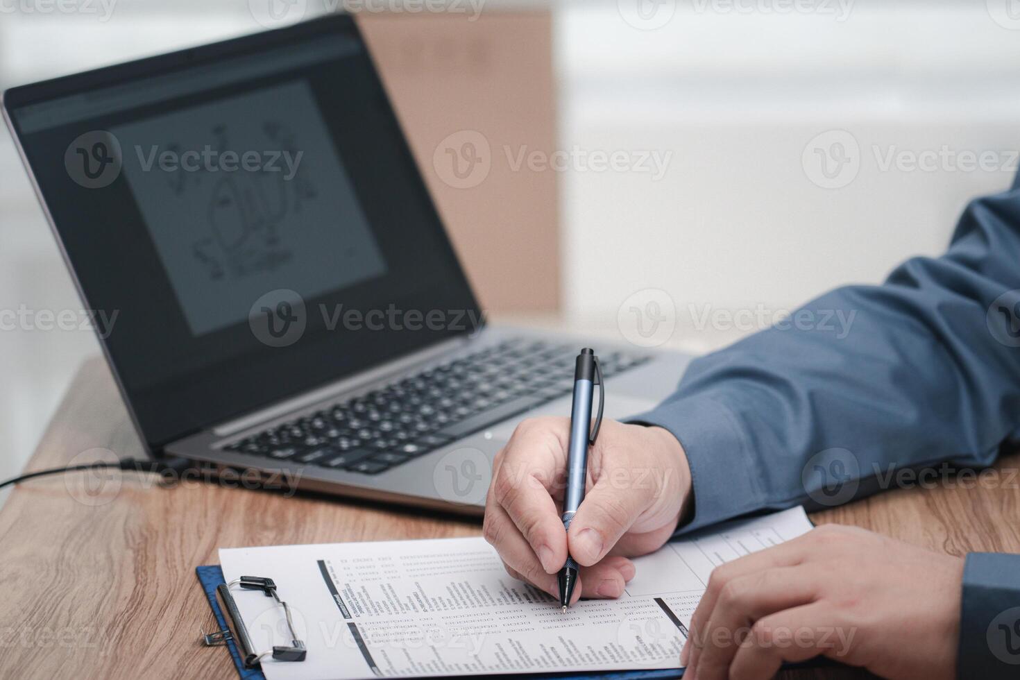 A man use a pen writing on the white paper clip board file in service concept and laptop on table in work office photo