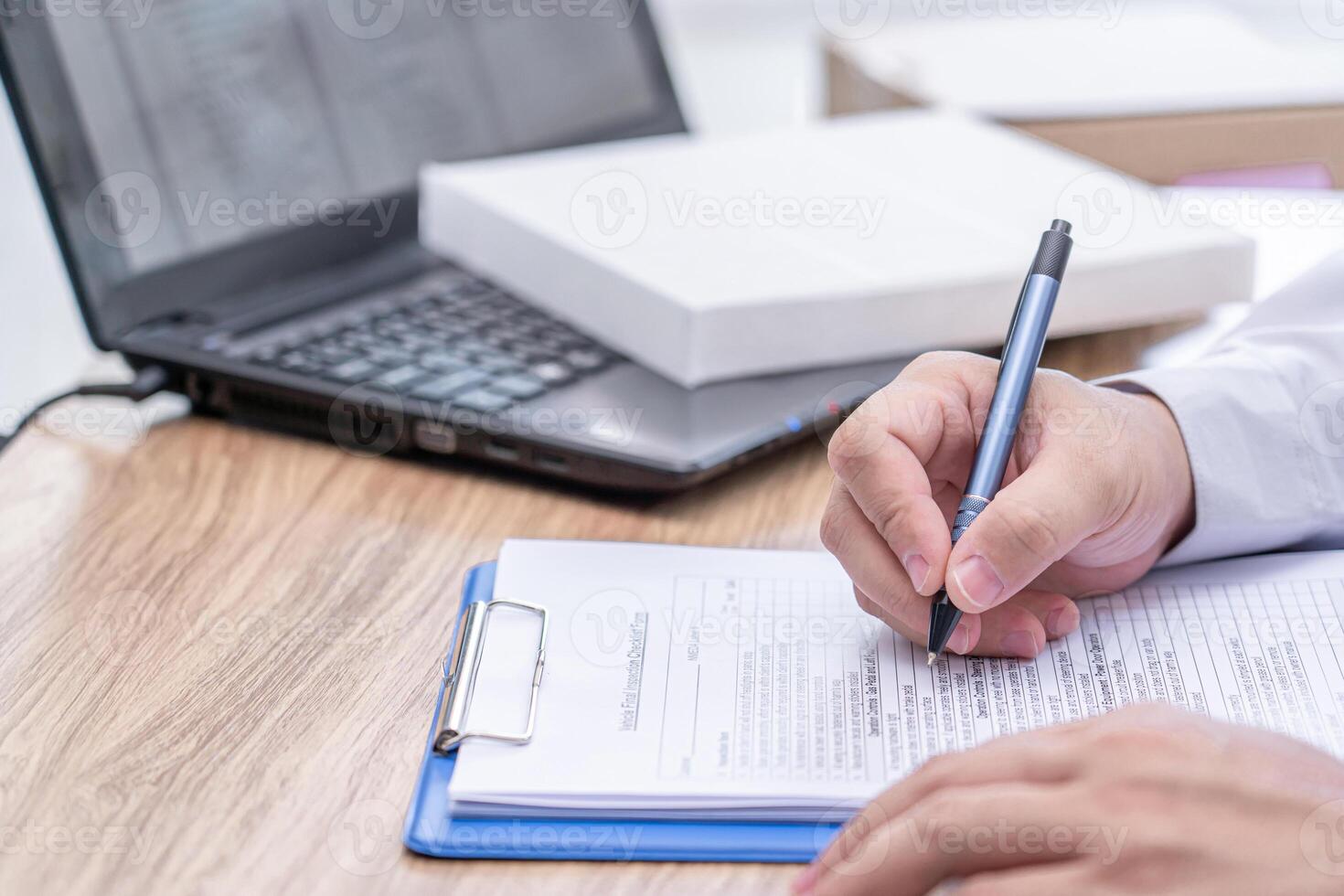 A man of car service center write on the clipboard paper check service list in office with new air filter of car cooling system and laptop computer on wood table photo