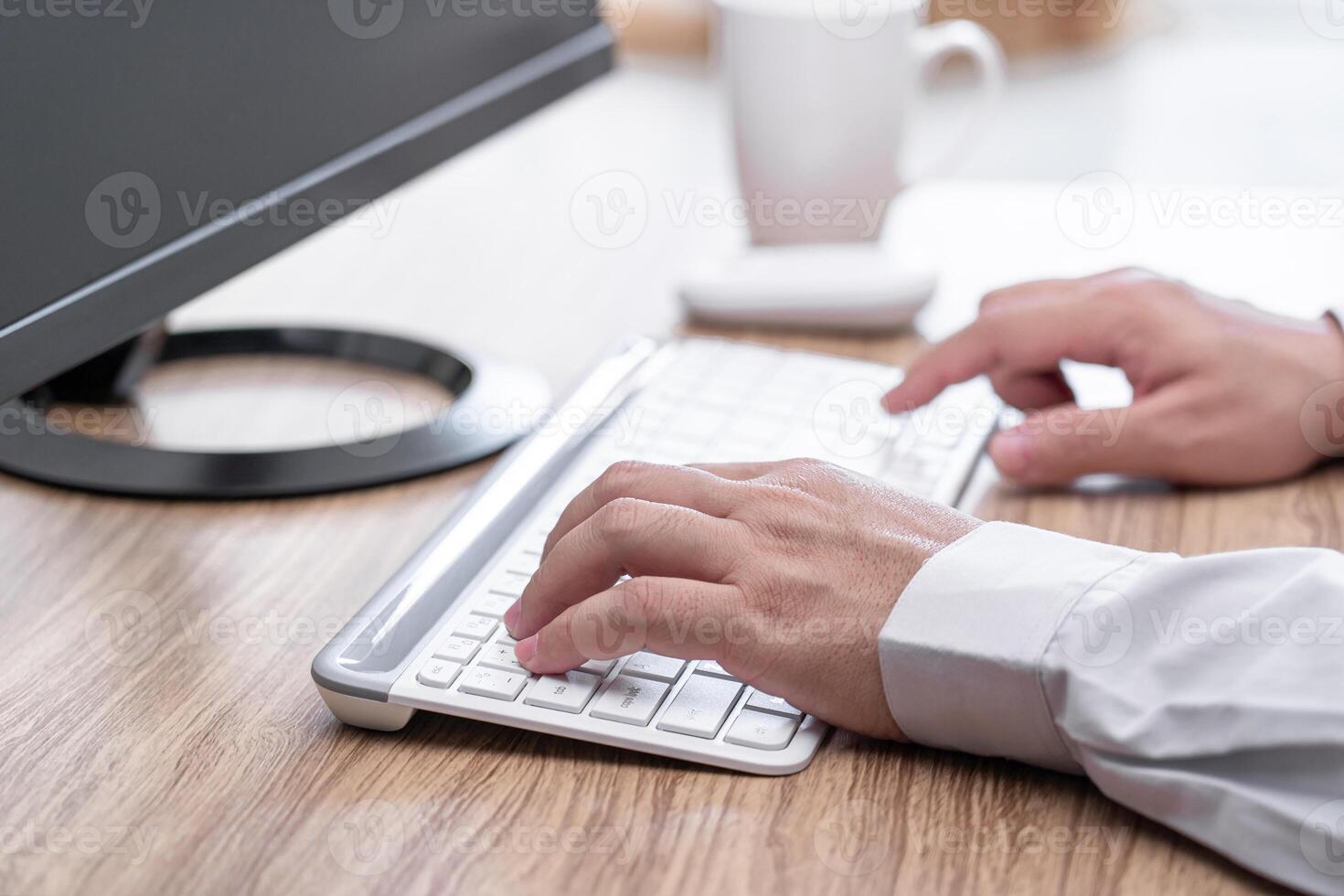A man typing on white desktop keyboard on wood table business work concept in office photo