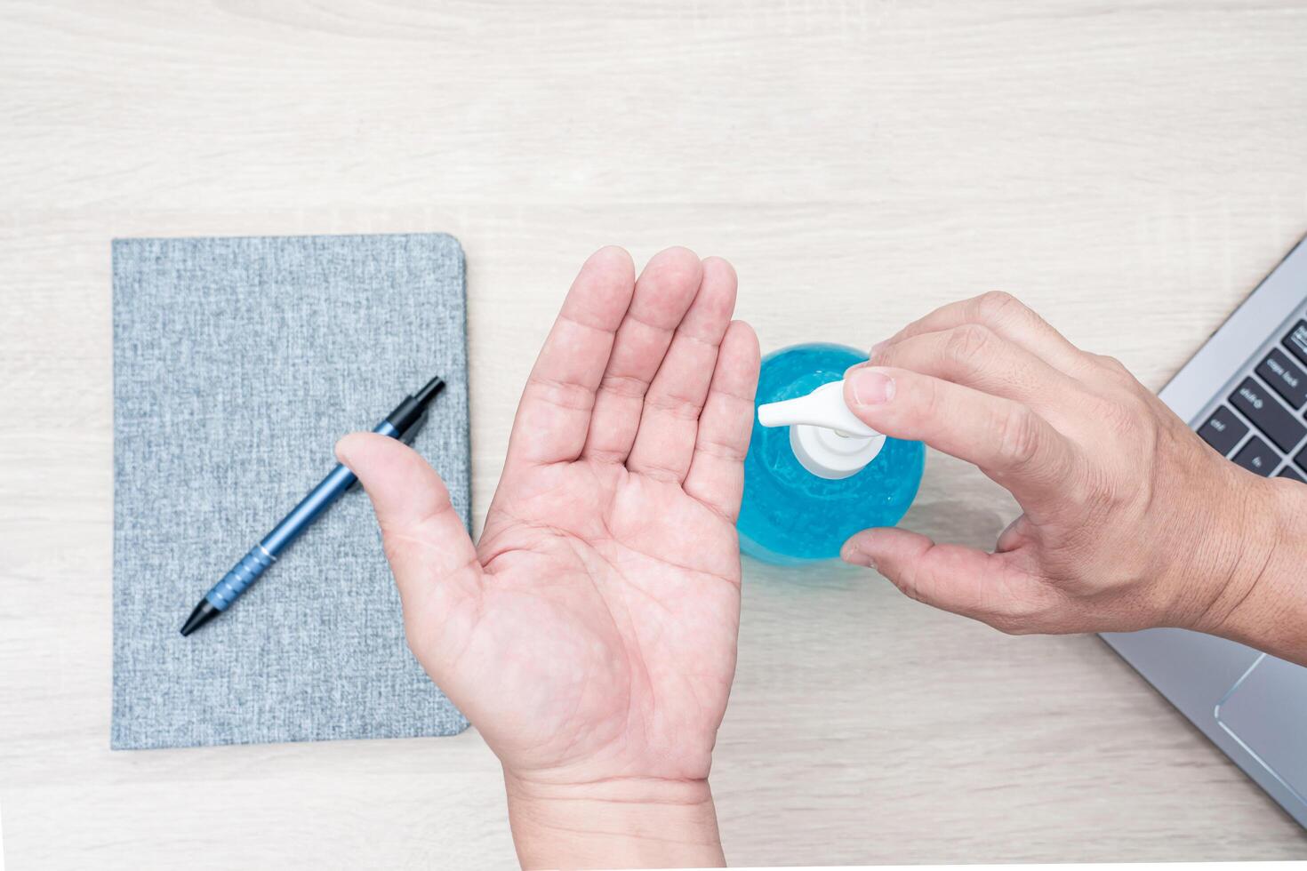 hombres utilizar alcohol gel para proteccion y limpieza un mano después utilizar computadora en madera mesa, trabajando a hogar concepto foto