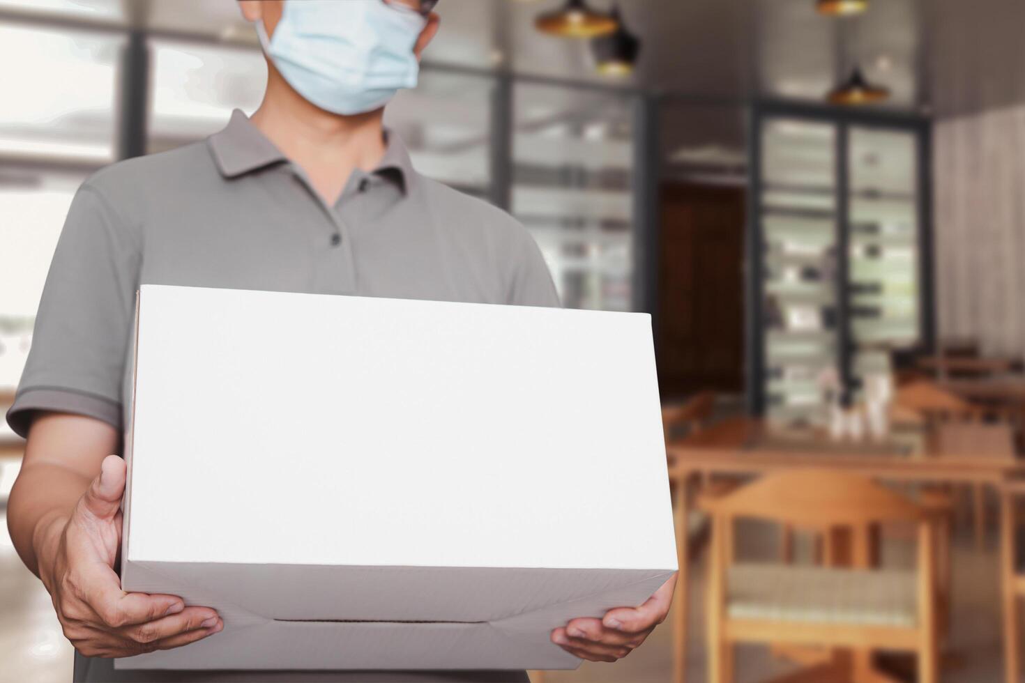 Delivery man shipping box wearing   protective mask for protection in delivery work with Restaurant background food home delivery concept photo
