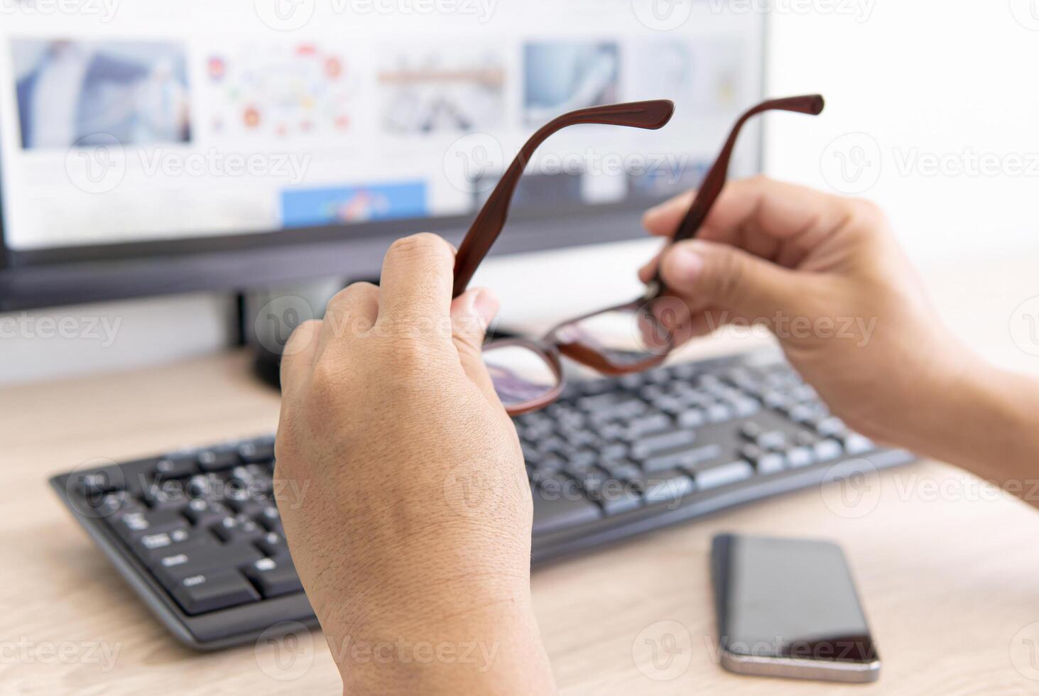 A man taking off glasses, feeling eye strain after long work with desktop computer on the wood table photo