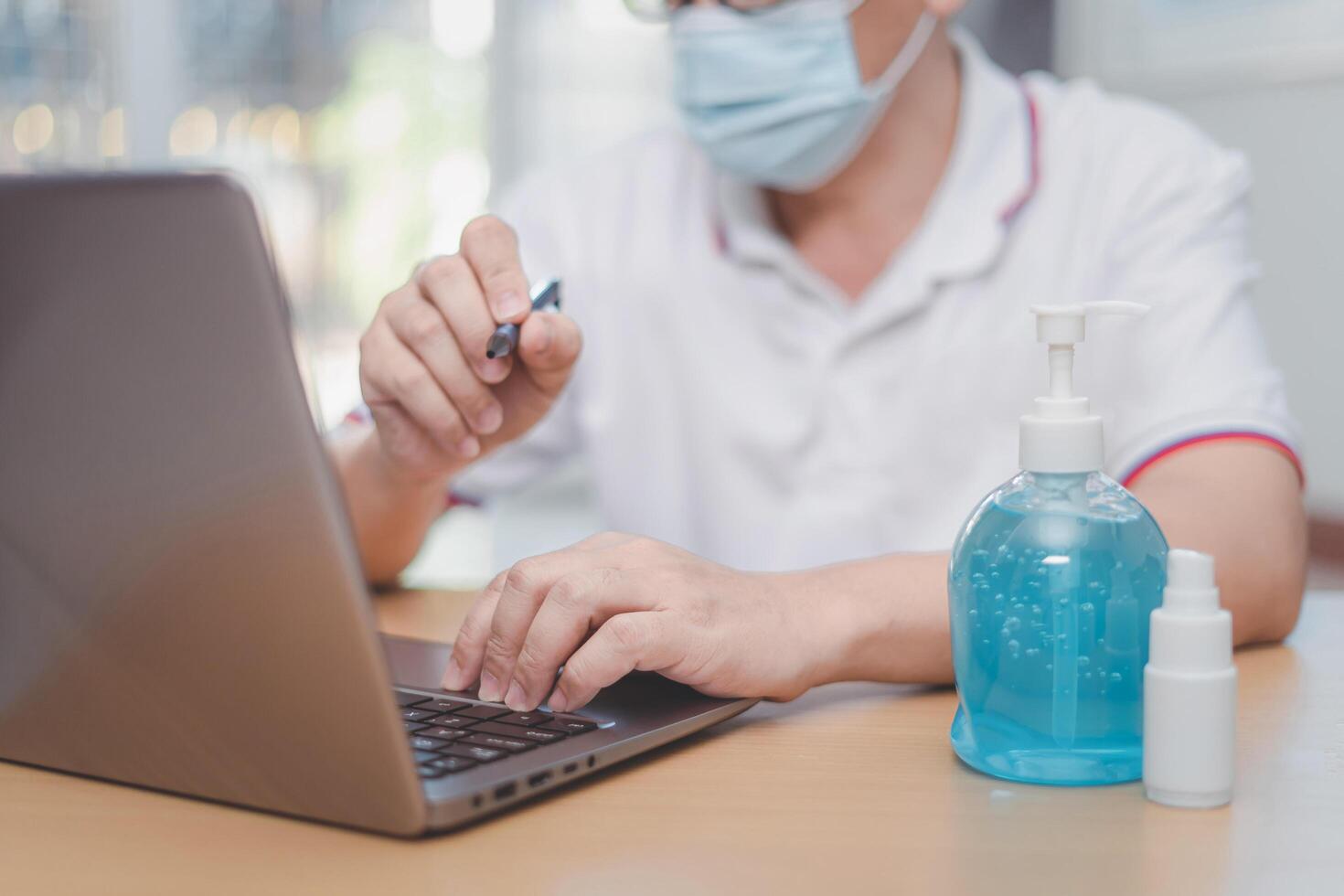 Work from home concept  Asia man wear a mask use laptop computer Find out about the spread of disease and use an clean and anti-virus alcohol spray and gel photo