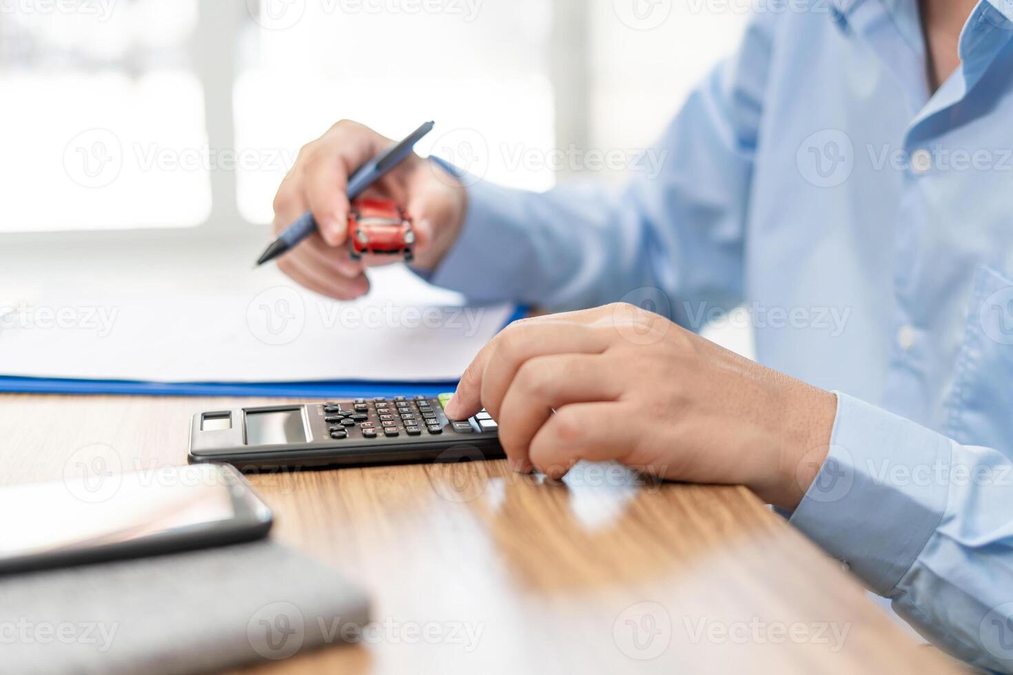 Car insurance concept Man use calculator pen and hold a accident toy car and write insurance documents on wood table photo