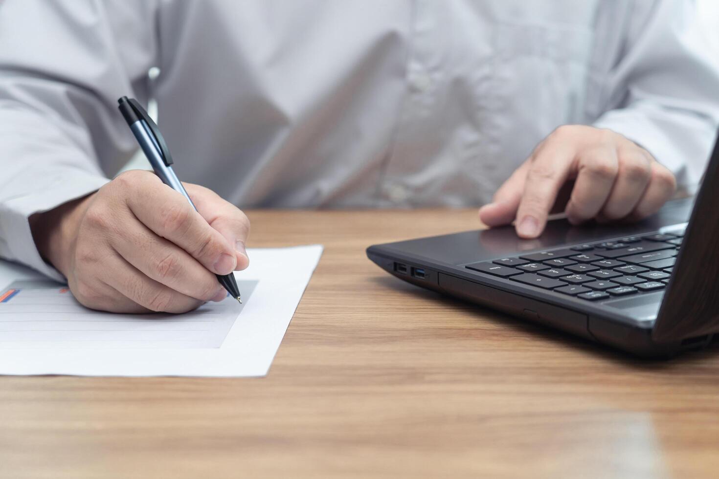 Man use pen write on a graph paper in work process everyday on table and use laptop computer in background photo