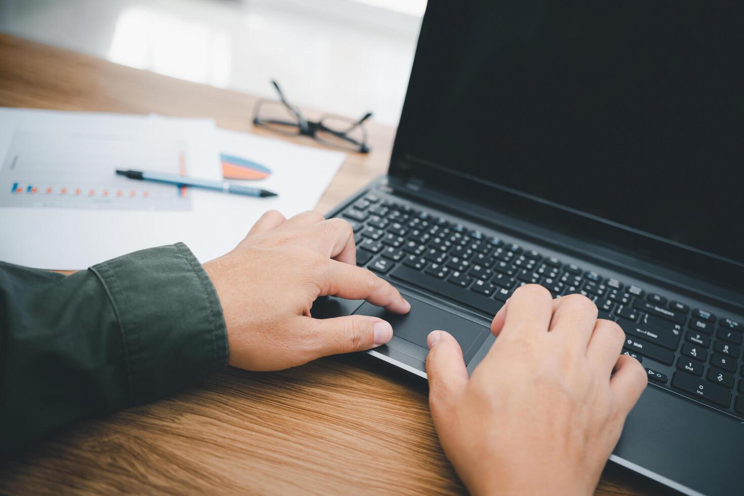 A man touch the mouse pad of laptop computer and typing on the keyboard in business work on the wood table photo