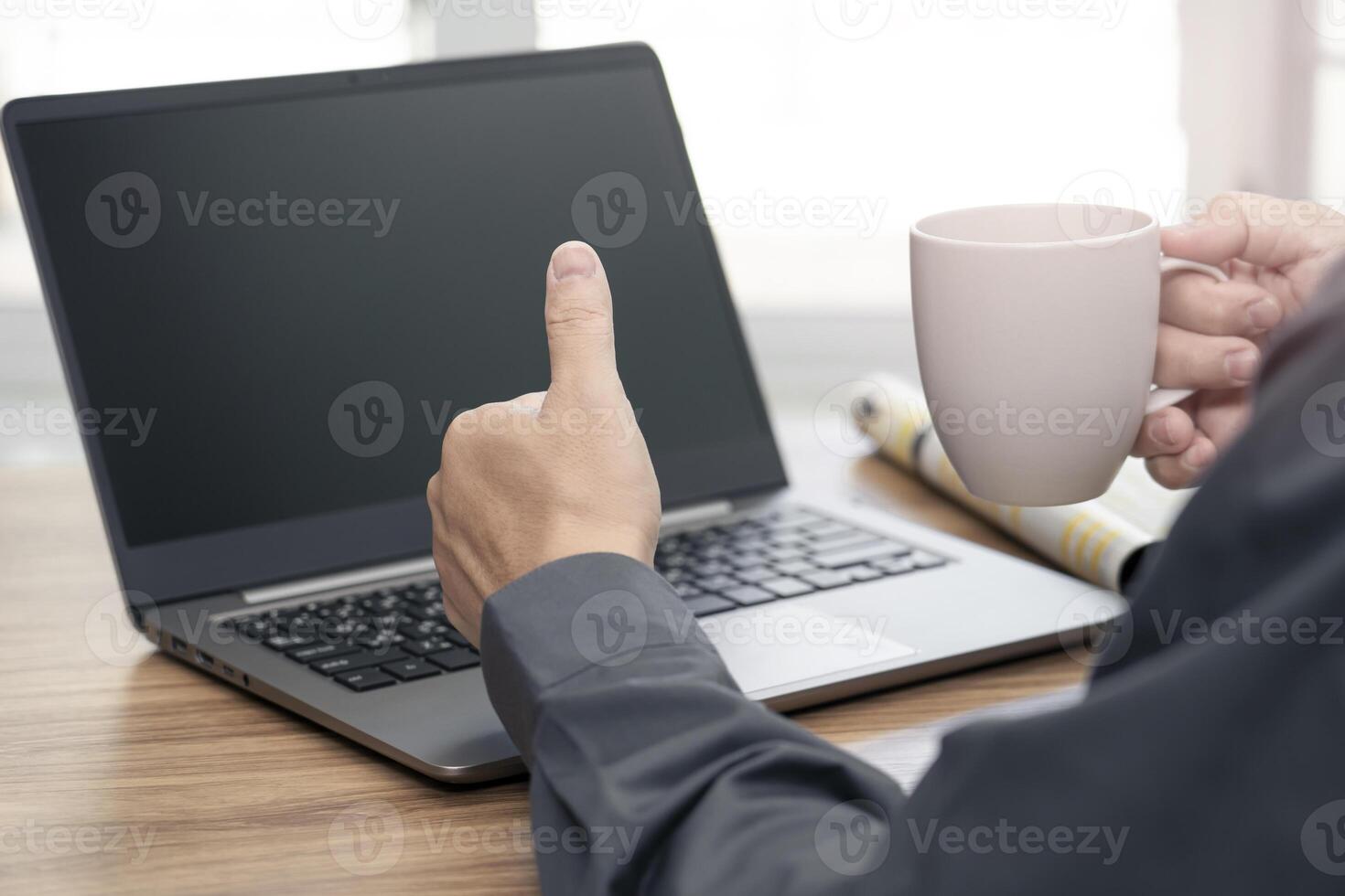 Close up hand Asia man thumbs up and drink coffee while using a laptop computer for an online meeting business work concept work from home photo