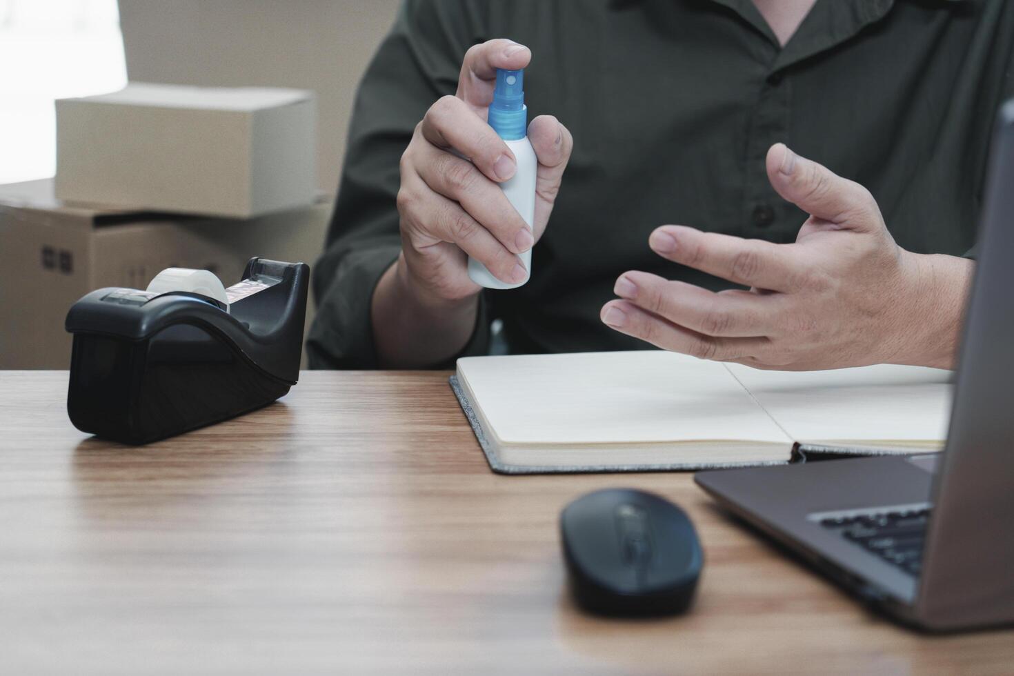 A man press alcohol bottle spray for clean hand cleaning before starting work to prevent the spread of germs delivery parcel box in background. entrepreneurial self employed business concept photo