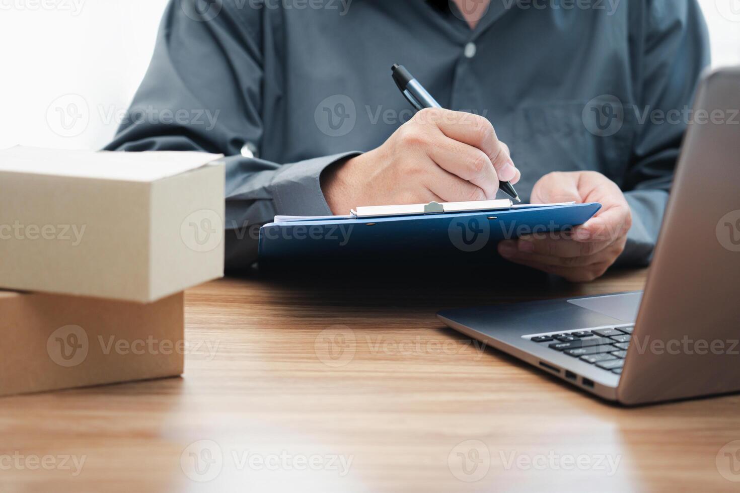 Postal man check order list for transport parcels and use laptop check stock order online order and write on the paper file photo
