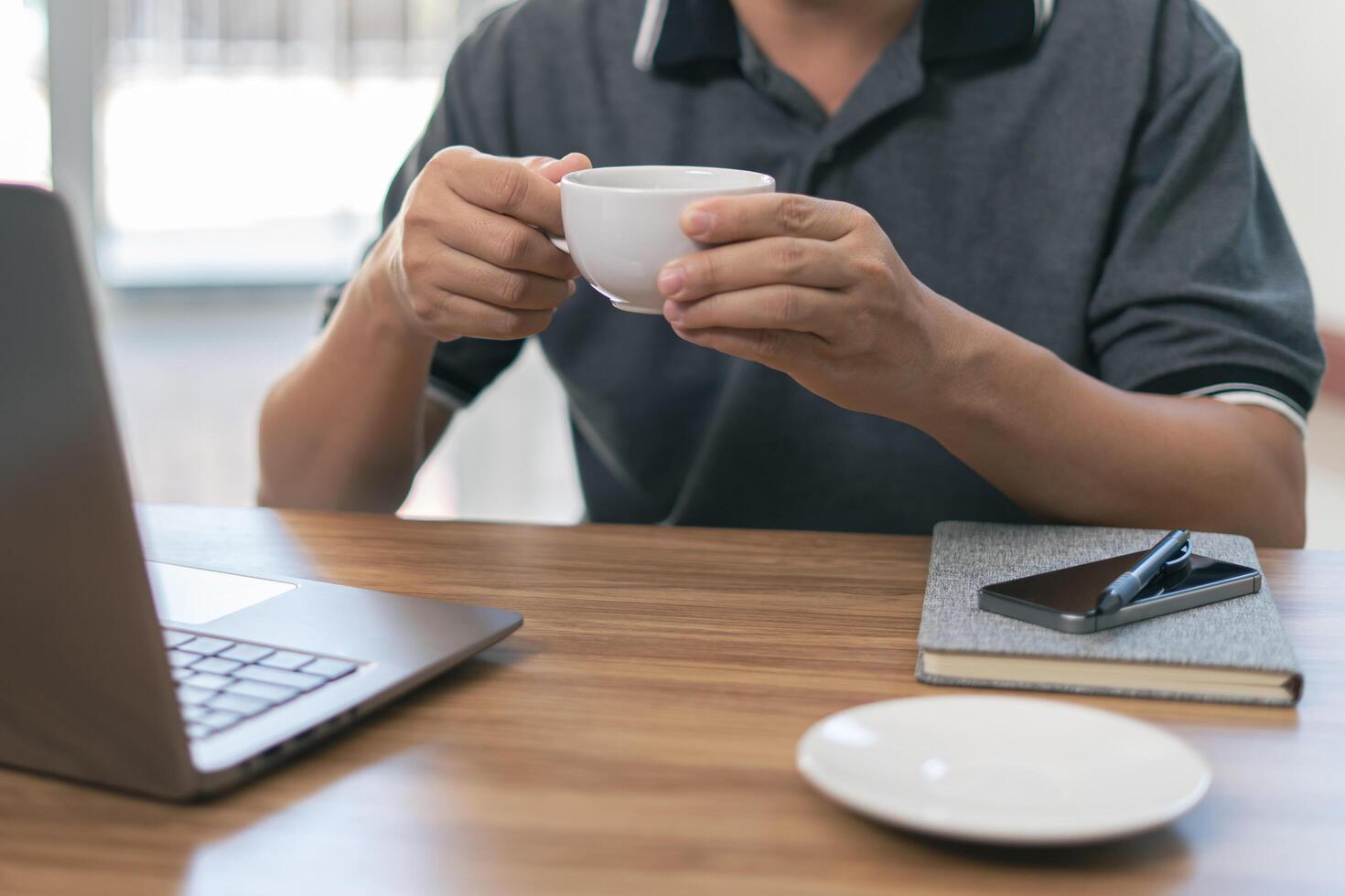 A man use right hand hold coffee mug drink coffee and use laptop computer on the wood table photo