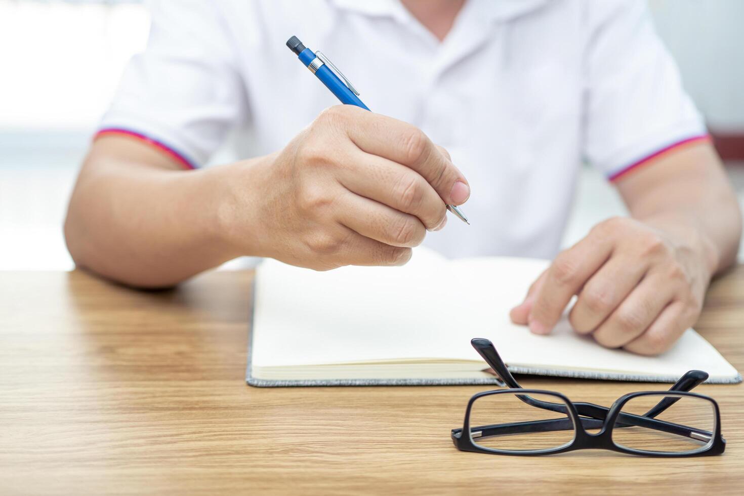 Asia man use pencil writing on notebook paper with glasses on the wood table in working concept photo