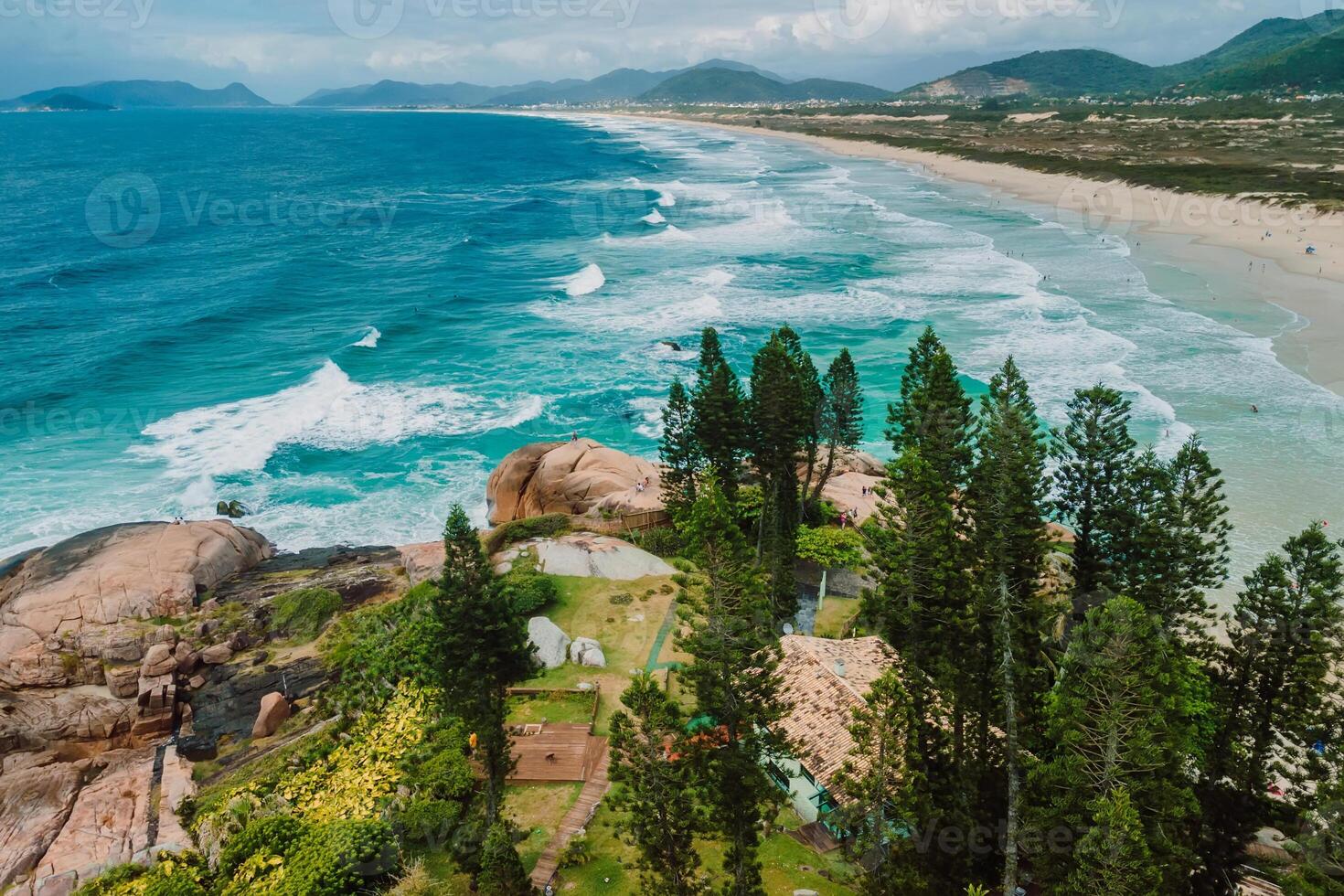 Joaquina beach with trees and ocean with waves in Brazil. Aerial view of coastline photo