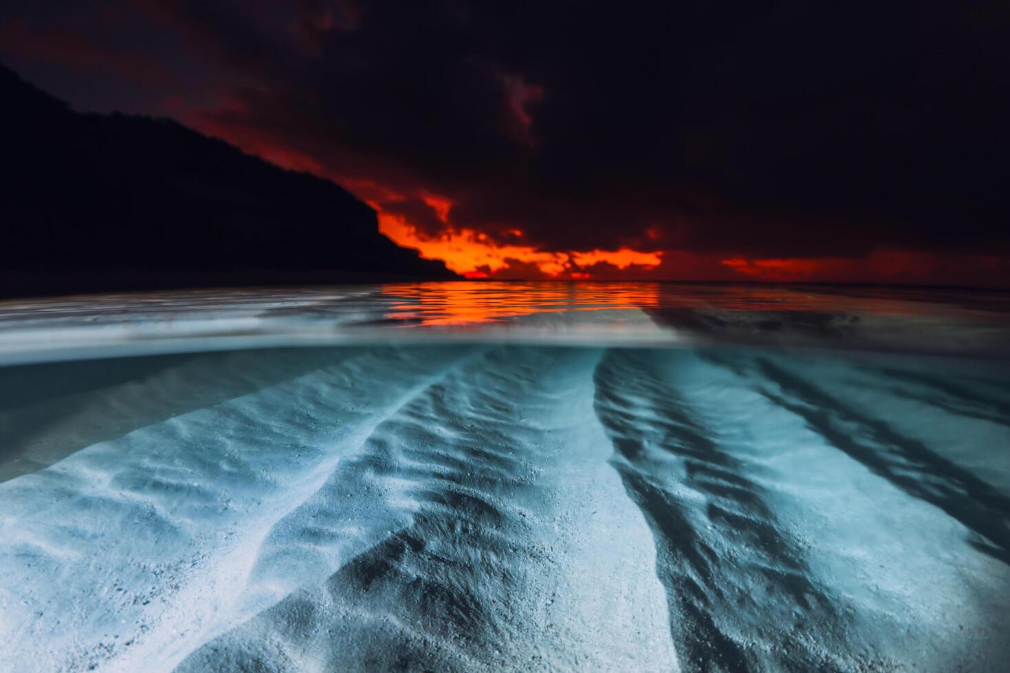 Split view with sunset or sunrise and underwater sandy sea bottom. Tropical sea with bright sunset or sunrise, underwater view with flash light photo