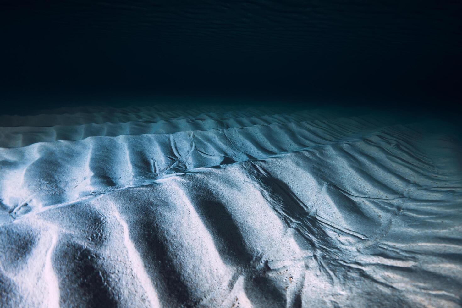 tropical claro azul Oceano con arena fondo en noche. submarino ver con artificial ligero foto