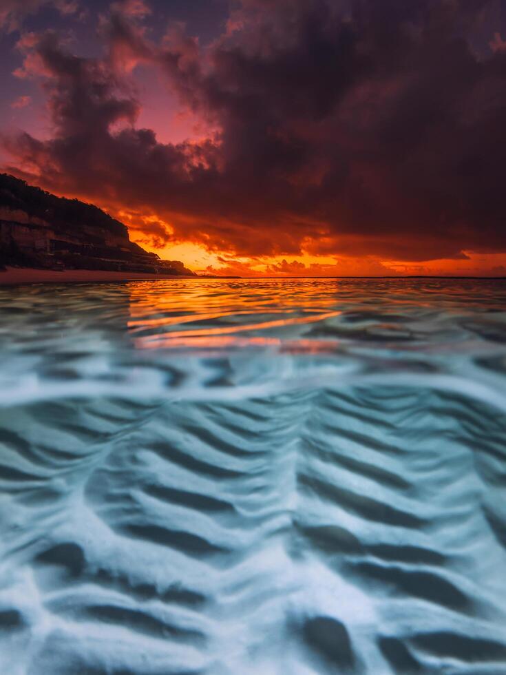 Split view with colorful bright sunset and underwater sandy sea bottom in tropical ocean. photo