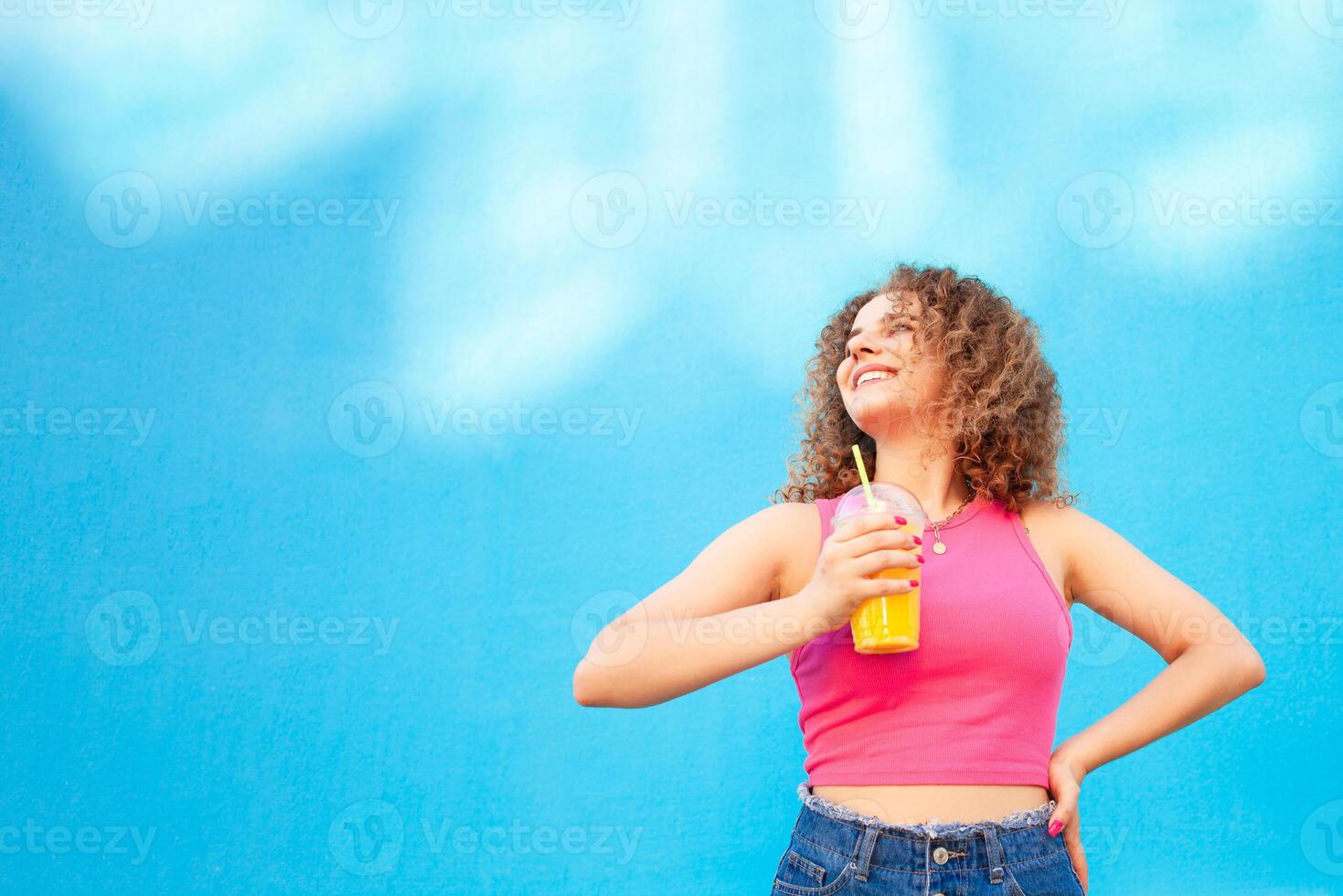 Beautiful happy woman with orange cold juice, concept summer drinks, rest and vacation. Blue background, isolated, copy space. Smiling, enjoying life, healthy and refreshing smoothie photo