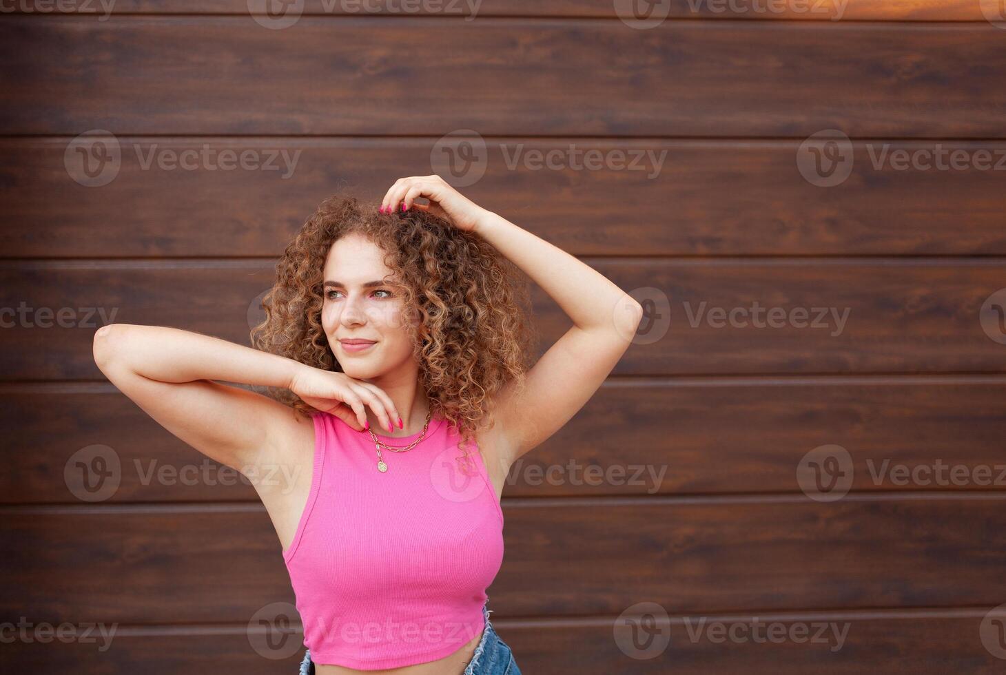 beautiful curly woman walks in city, against backdrop of brown wall, copy space for text. Happy, cheerful, smiling. portrait. photo