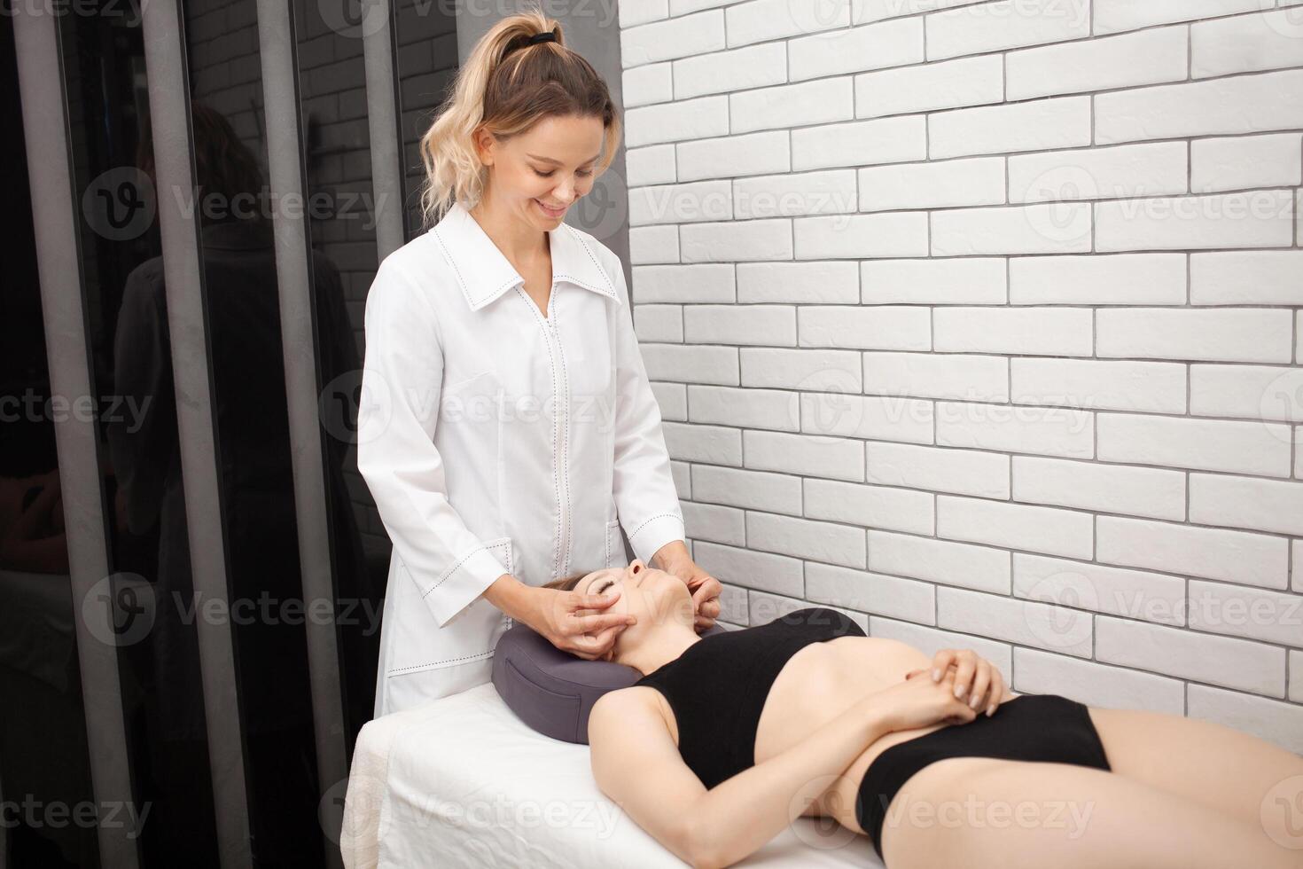 cosmetóloga lo hace mujer facial masaje con su manos, relajación y placer, piel corrección, levantamiento. sonriente foto