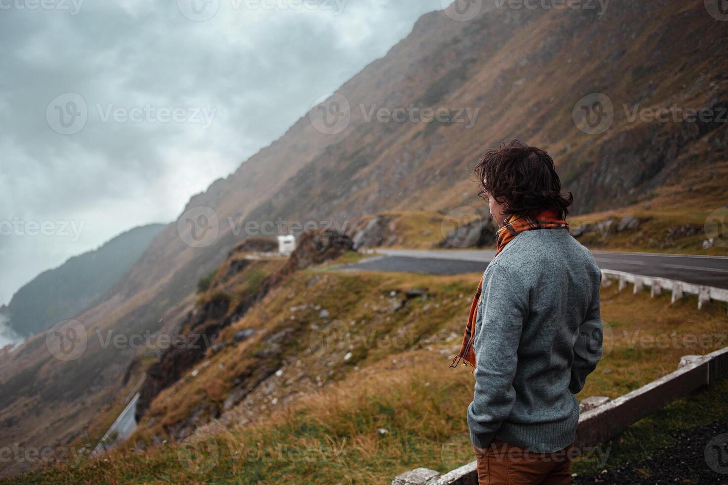 man stands on road in mountains in Romania, Carpathians. concept of loneliness, freedom, melancholy and thoughtfulness. Autumn, rain and fog, nature, outdoors. Man and nature, landscape, cold. photo