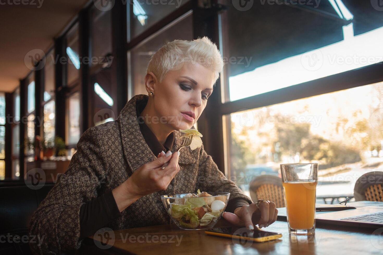 mayor mujer de 50 años es hermosa y elegante, se sienta en cafetería, trabajos con computadora portátil, Lanza libre diseñador. mira excelente, contento vida, activo estilo de vida. almuerzo, bocadillo. foto