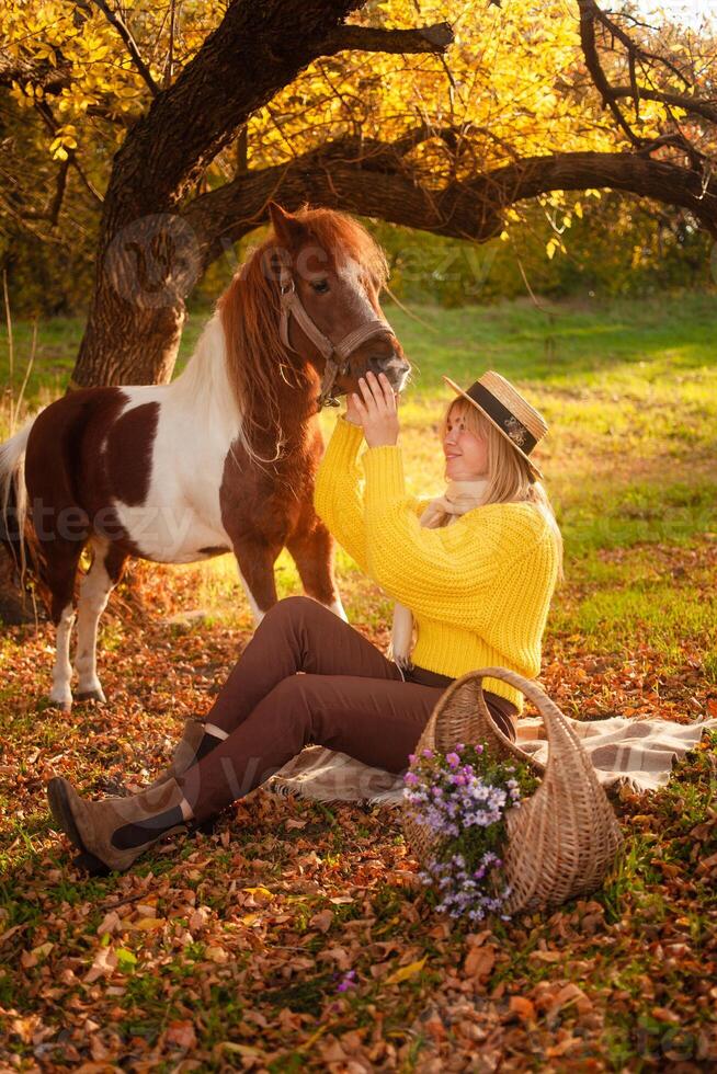 woman and spotted brown pony at sunset in forest, beautiful girl in autumn clothes loves her horse, concept of kindness, animal care, nature and friendship. Funny. photo
