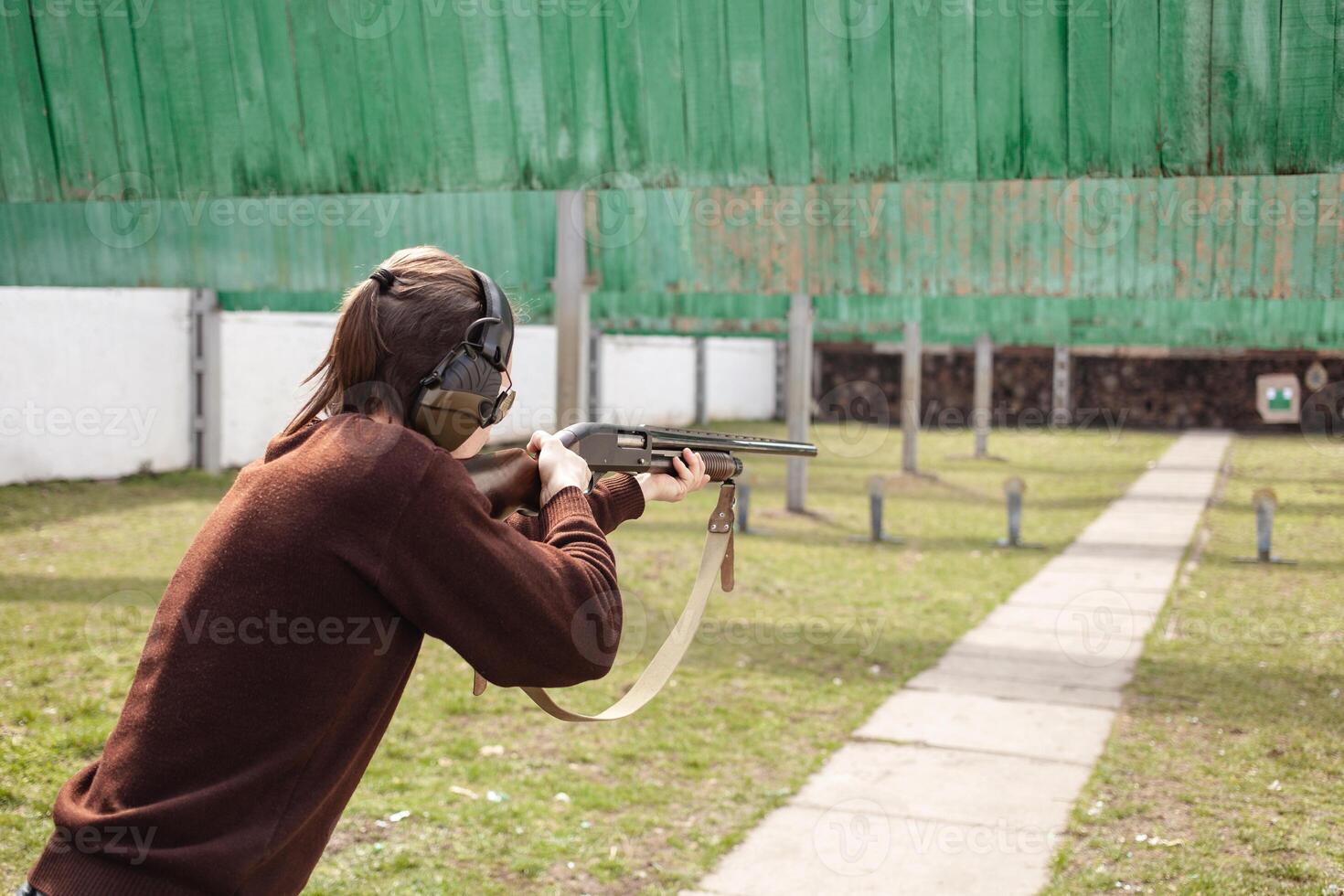 A man shoots at metal flags, targets. Firearms pump-action shotgun. Tyre's outdoor. Patrons with a fraction. Green grass, a man with headphones, a glade with protection for shooting. close up photo