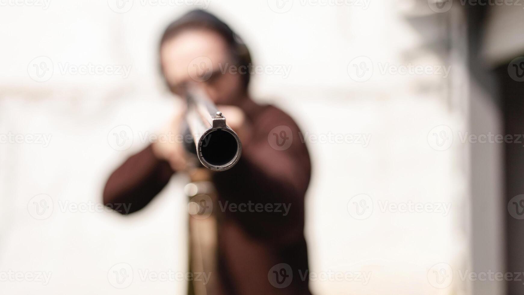 A man with a pompous firearm on a white background. A man in protective glasses and headphones. Tyre outdoor. Grey hangar. gun copy space photo