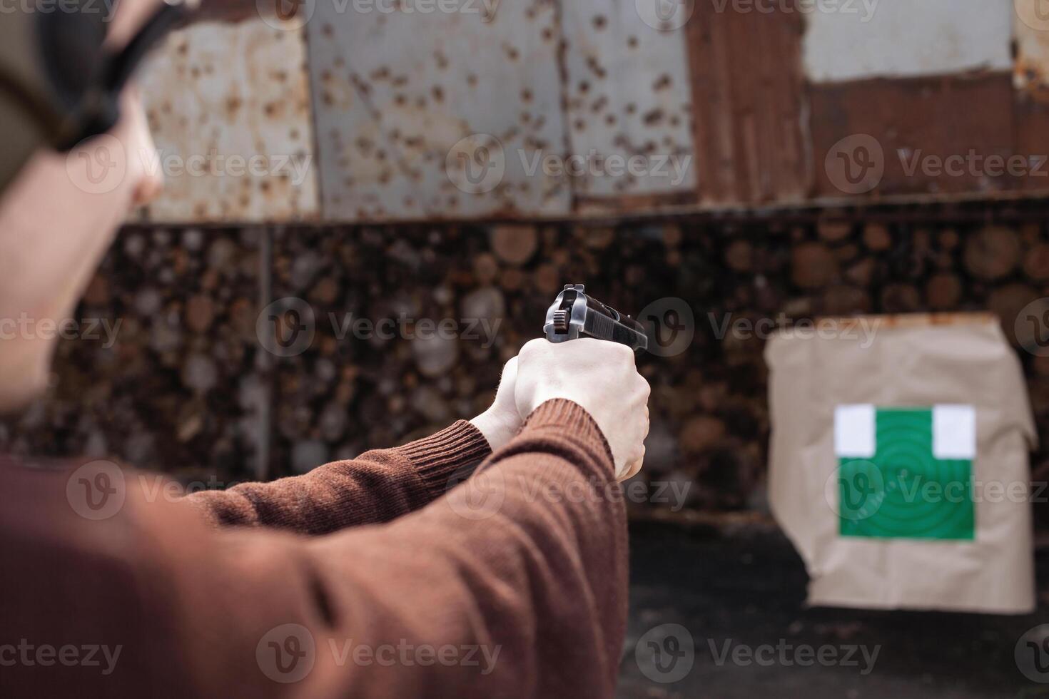 A man shoots a gun, aiming at the target. A man wearing protective headphones. A wall and a roof with bullet holes. outdoor shooting range photo