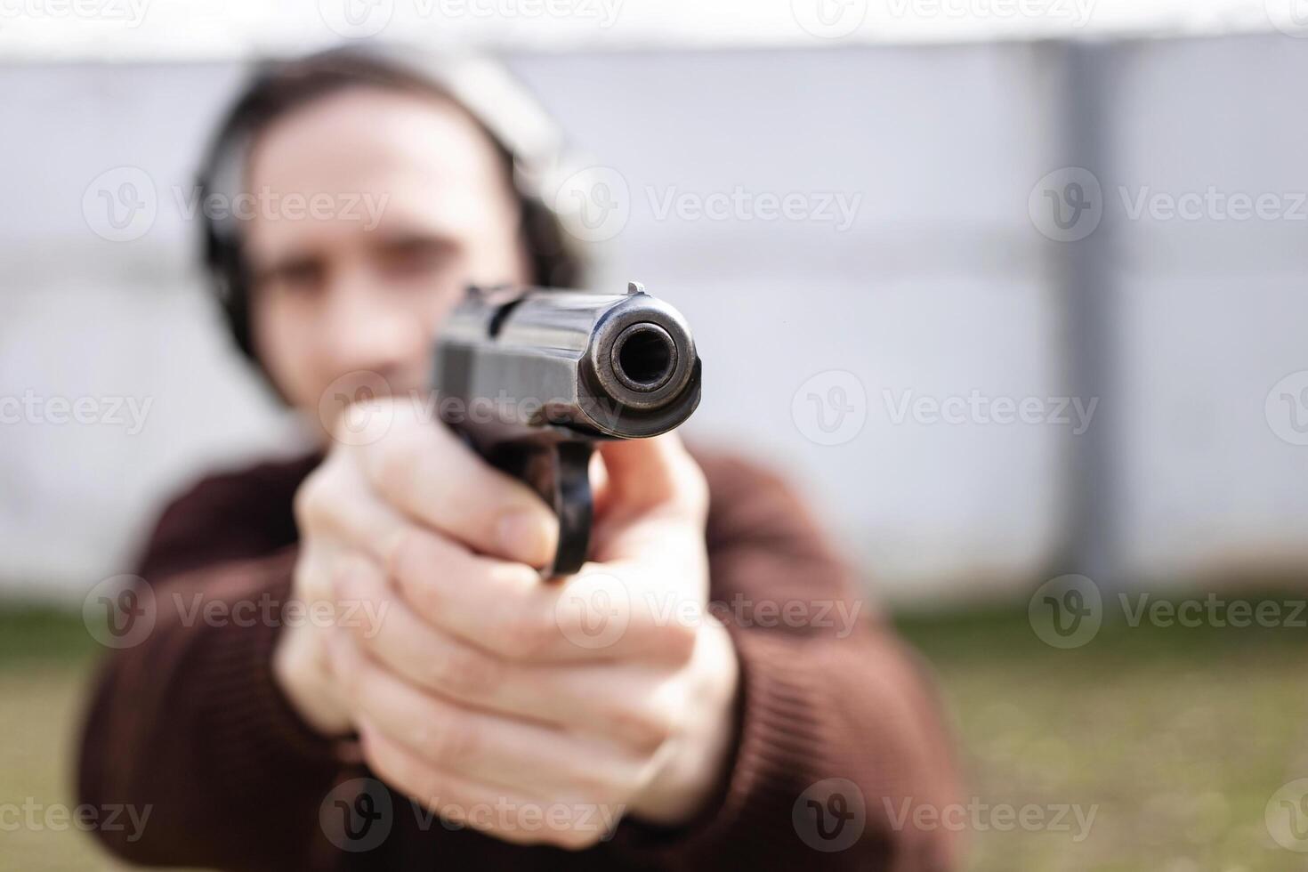 un hombre es puntería para un pistola. un hombre vistiendo protector auriculares. al aire libre neumático disparo rango. pasatiempo. arma de fuego en contra el blanco pared Copiar espacio foto