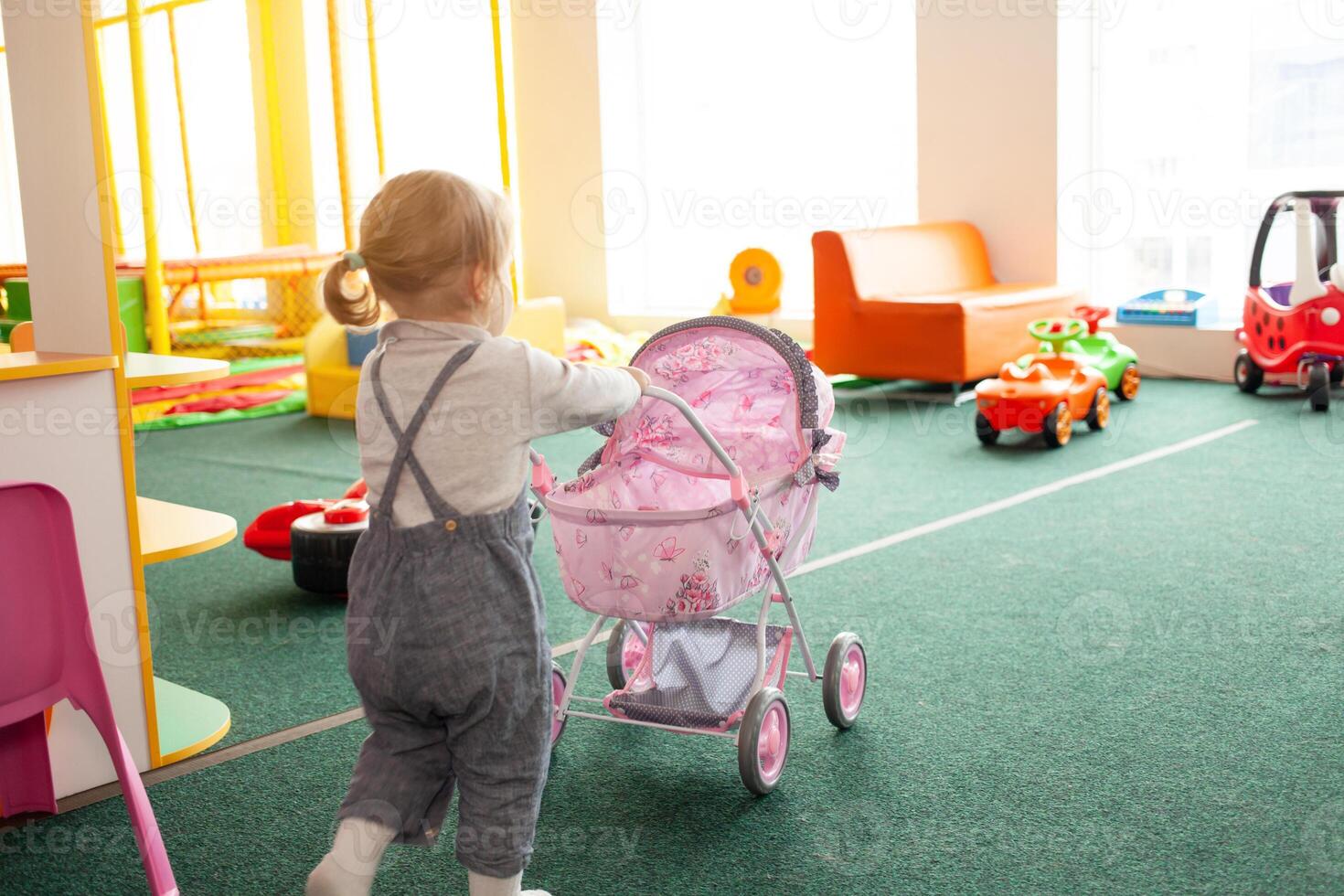 A small two-year-old girl plays with toys in the playroom photo