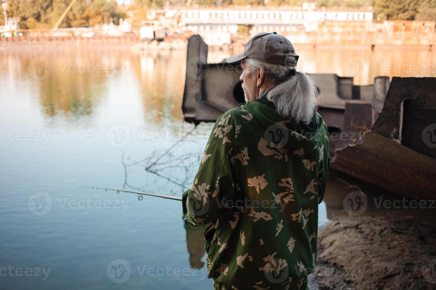 older man is fishing on the river. Dirty water, pollution, garbage, rusty barges. Ecological catastrophe, production waste. photo