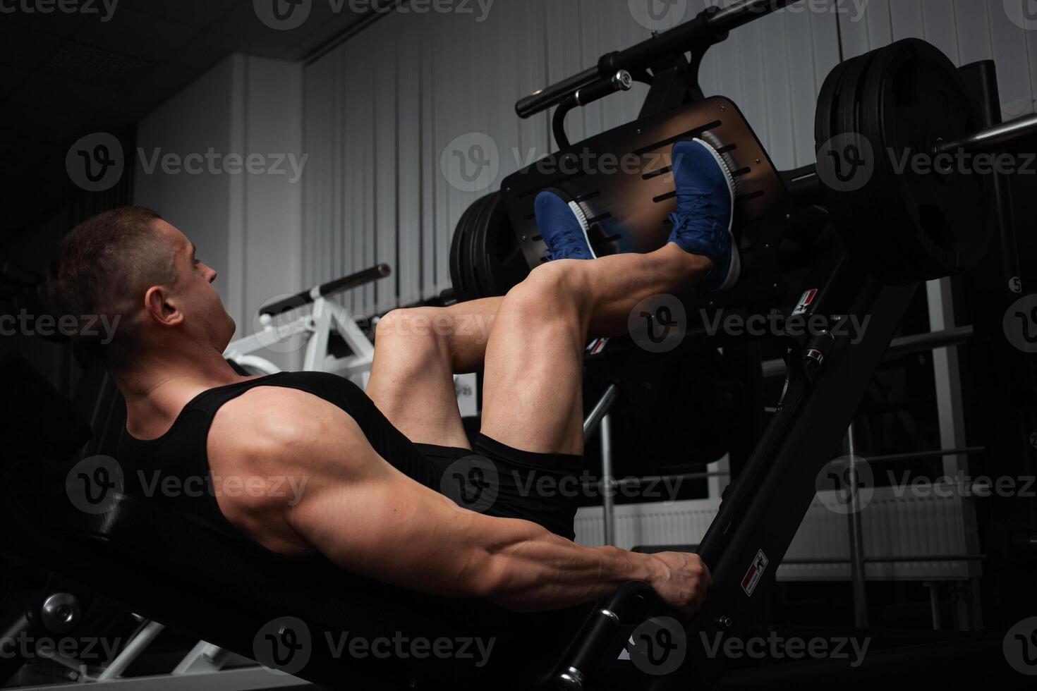 portrait of a handsome male coach in gym. The athlete does an exercise on the simulator in the gym. Builds muscle, plays sports, a healthy lifestyle. squeezes weight with legs photo